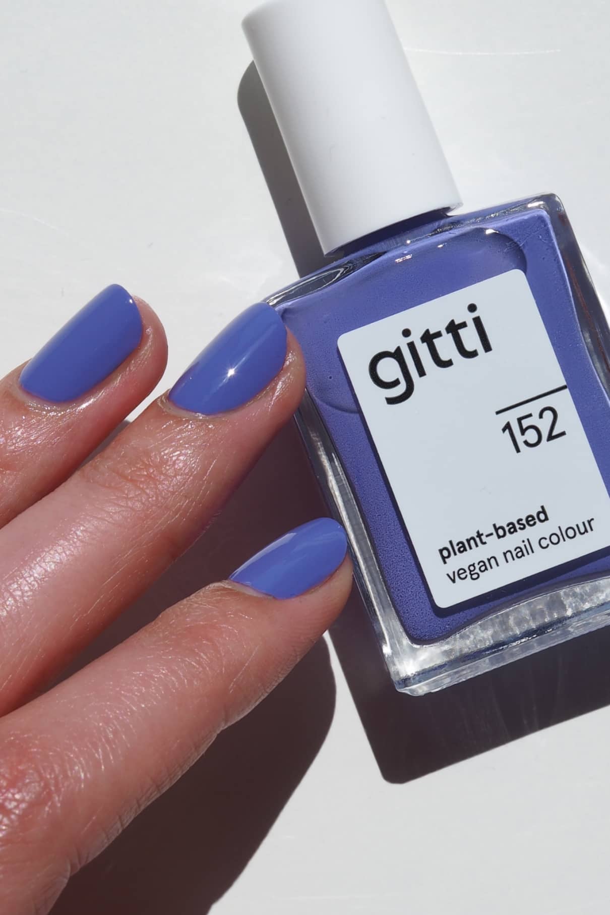 Eine Hand mit in blaustichigem Violett lackierten Nägeln ruht neben einer Flasche gitti no. 152, einem veganen Nagellack auf pflanzlicher Basis in einem passenden Farbton.