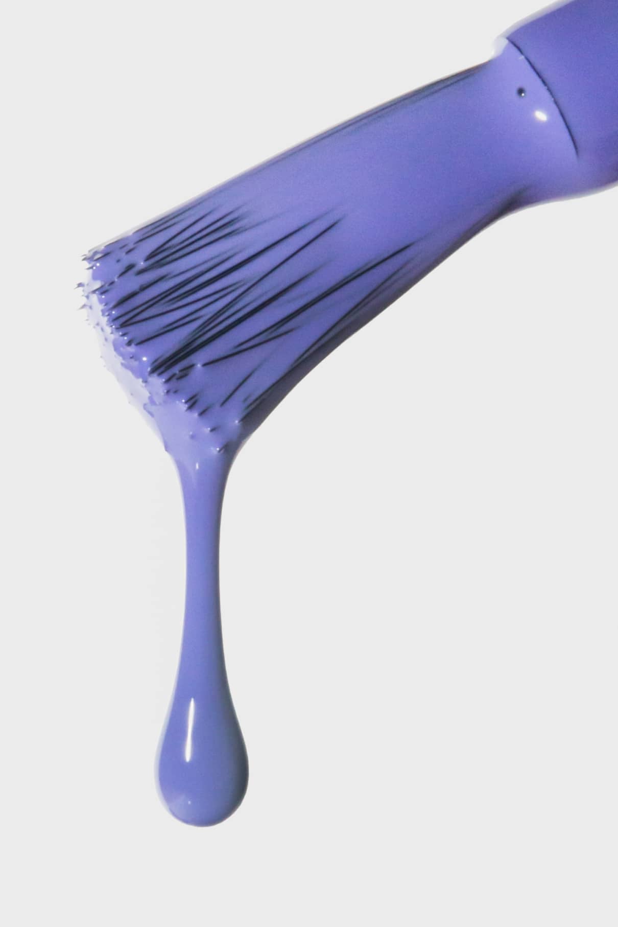 Nahaufnahme eines Pinsels mit gitti no. 152, eine Ode an die Pantone Farbe des Jahres 2022, mit einem großen violetten Tropfen, der von den Borsten herabhängt, vor einem weißen Hintergrund.