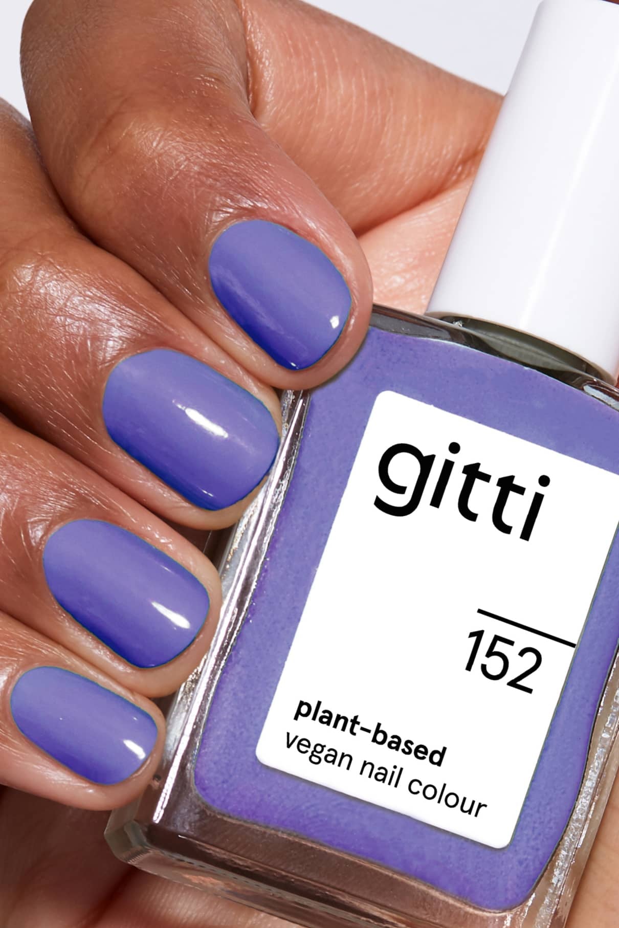 Eine Hand mit kurzen, sauber manikürten Nägeln, die in einem bläulichen Violett lackiert sind, hält eine Flasche mit gitti no. 152, einer veganen Nagelfarbe auf Pflanzenbasis, die von Pantones Farbe des Jahres 2022 inspiriert wurde.
