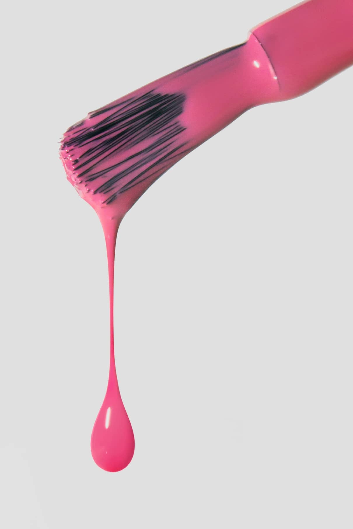 Eine Nahaufnahme eines Nagellackpinsels, der mit Gitti Nr. 154, einem warmen rosa Farbton, mit einem einzelnen Tropfen, der auf einen schlichten weißen Hintergrund fällt.