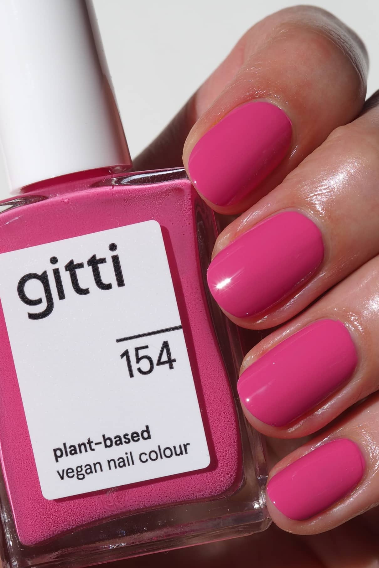 Eine Hand mit kurzen, sauber manikürten Nägeln, die in einem warmen Pink lackiert sind, hält ein Fläschchen mit gitti no. 154, einer veganen Nagelfarbe auf Pflanzenbasis.