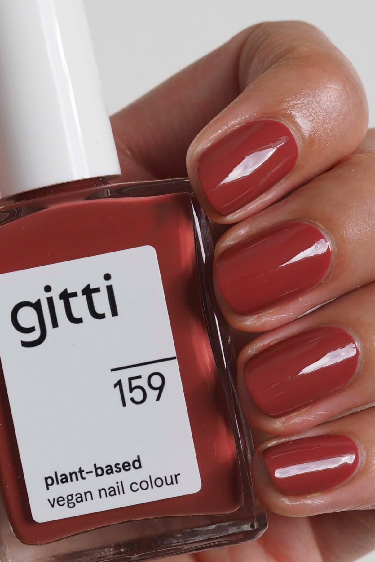 Eine Hand mit sauber manikürten Nägeln, die mit gitti no. 159, einer veganen Nagelfarbe auf pflanzlicher Basis in pudrigem Rot, hält die beschriftete Flasche.
