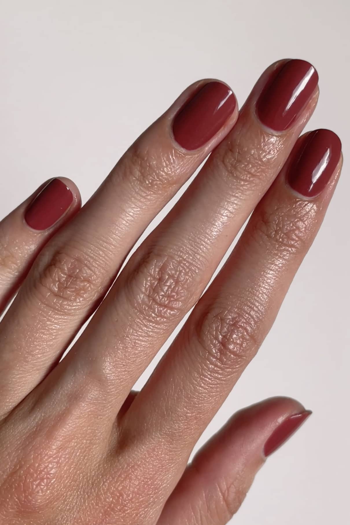 Eine Hand mit sauber manikürten Nägeln, die mit Gitti Nr. 159, einem glänzenden pudriges Rot (tiefes Rotbraun), ist vor einem schlichten hellen Hintergrund abgebildet.