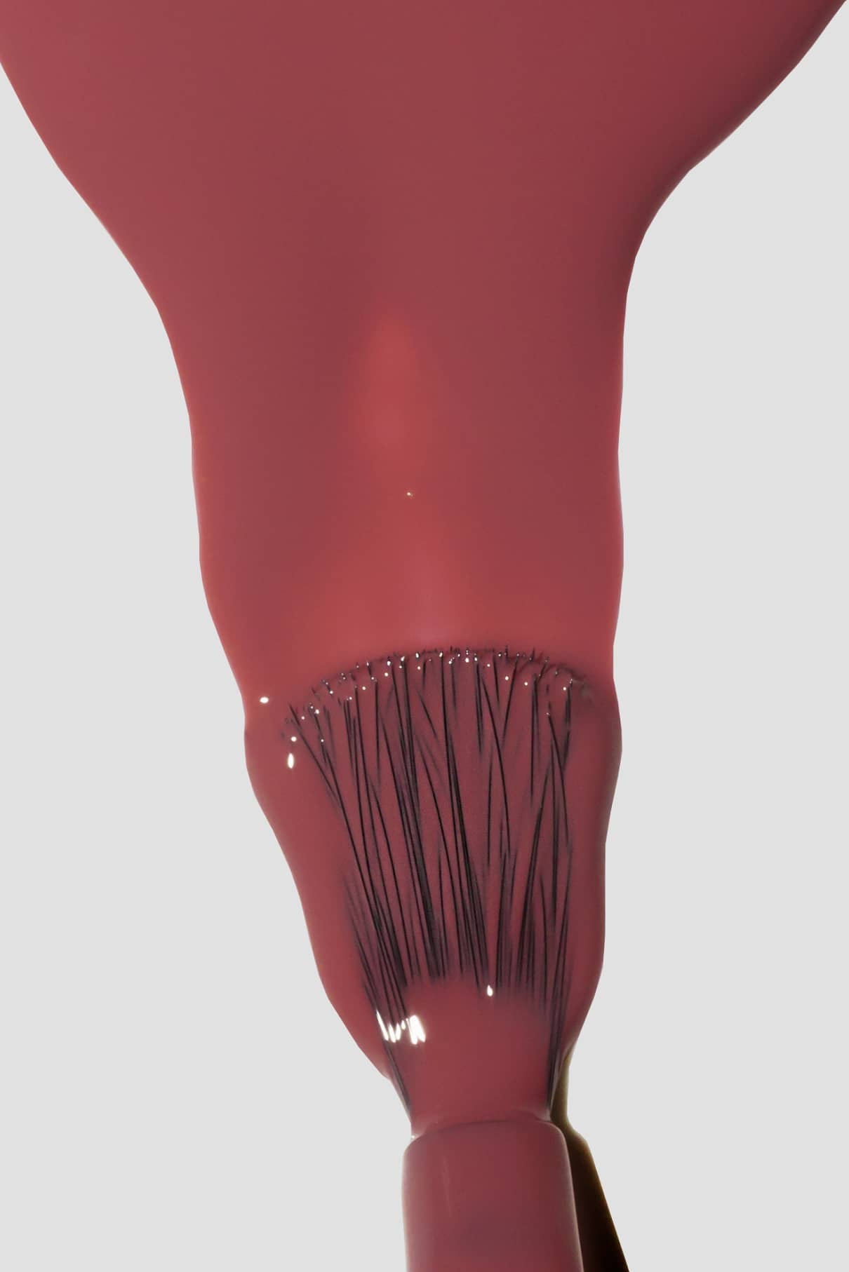 Nahaufnahme eines Pinsels, der gitti no. 159, ein glänzender, pudriges Rot-Pink-Nagellack, mit sichtbaren Borsten durch die durchscheinende Farbe vor einem hellgrauen Hintergrund.