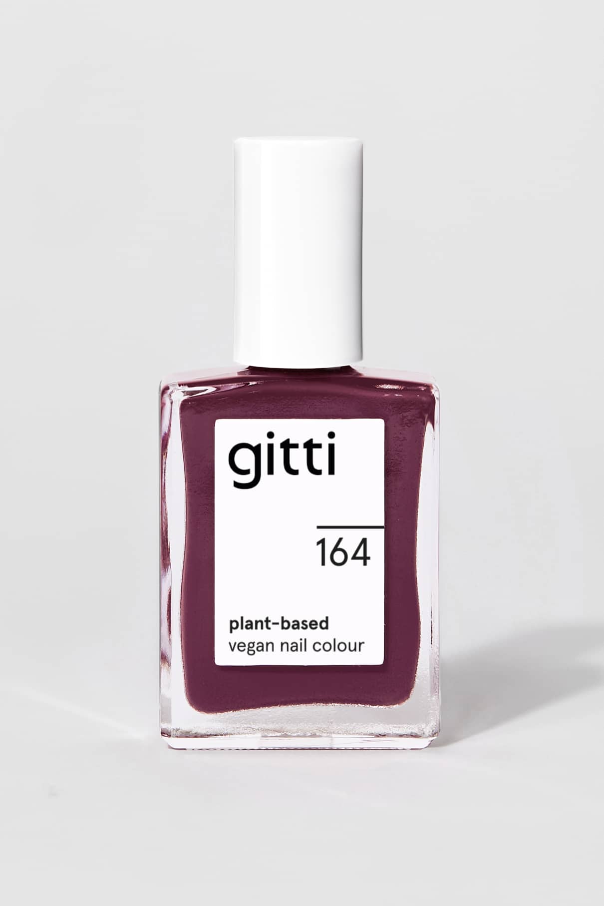 Eine Flasche gitti no. 164, ein pflanzlicher veganer Nagellack in rötlichem Lila mit blauen Untertönen, weißer Kappe und Etikett, vor einem schlichten hellen Hintergrund.