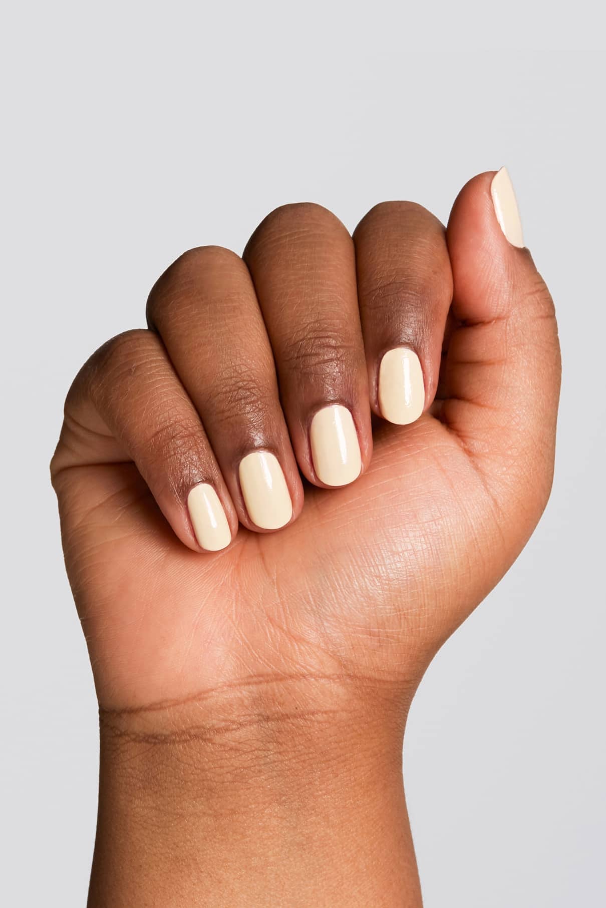 Eine Hand mit mittelbraunem Hautton ist in einer Faust abgebildet und zeigt kurze Nägel, die mit gitti no. 165, einem hellen Creme Nagellack mit gelben Untertönen.