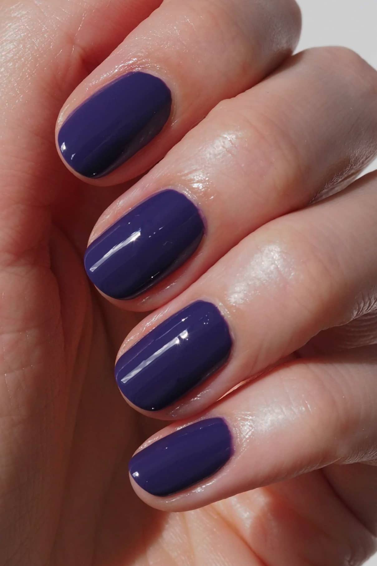 Eine Hand mit sauber manikürten Nägeln, lackiert in der glänzenden, dunklen Lila-Farbe von gitti no. 168.