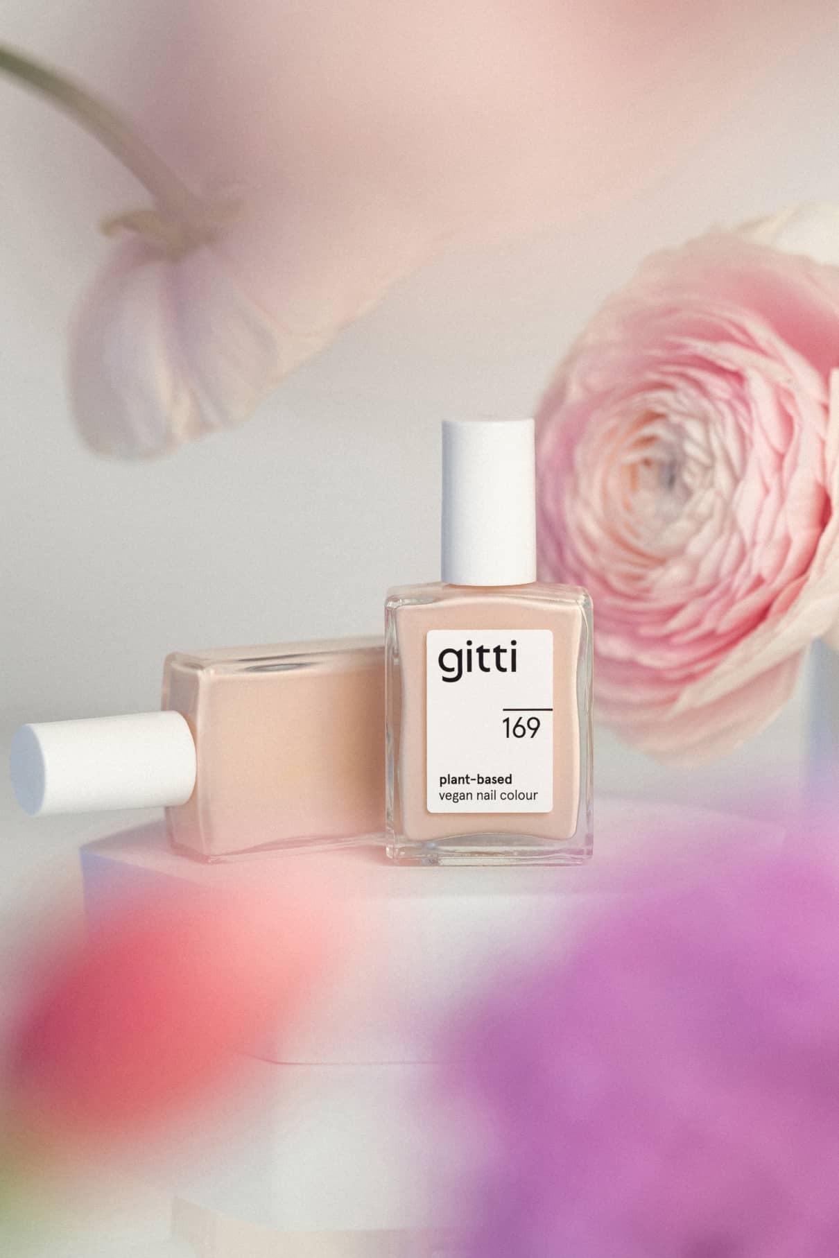 Zwei Flaschen gitti no. 169 pflanzliche, vegane Nagelfarbe im eleganten Farbton Roséton werden inmitten von rosa und violetten Blumen mit sanftem Fokus präsentiert.