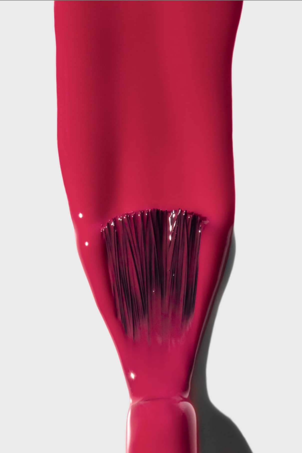 Eine Nahaufnahme eines Pinsels, mit dem gitti no. 170, ein magentaroter Nagellack, auf eine glatte weiße Oberfläche auf, wobei die leuchtende Farbe im Kontrast zu den sanften, gedeckten Tönen hervorgehoben wird.