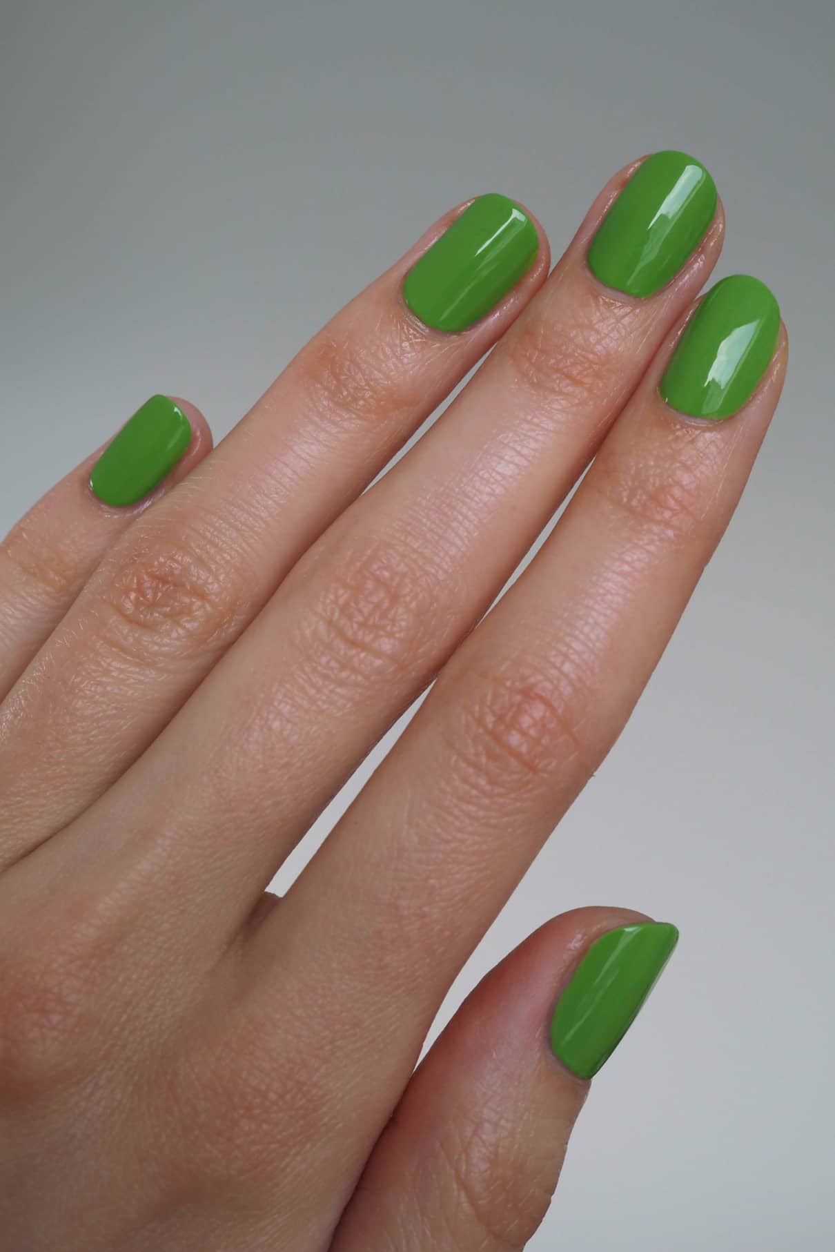 Eine Hand mit sauber manikürten Nägeln, lackiert mit glänzendem gitti no. 171, einem frischen grasgrünen Nagellack, vor einem neutralen Hintergrund.
