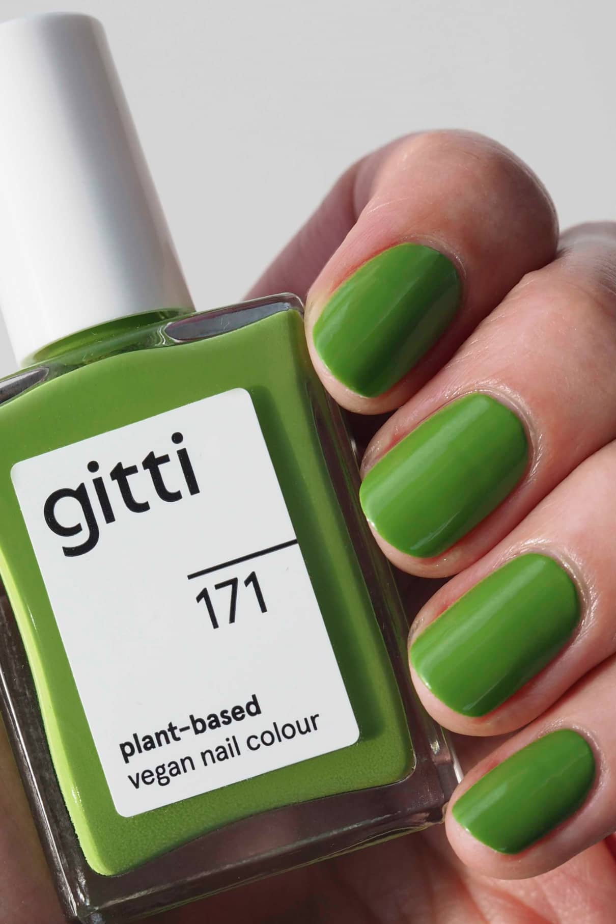 Eine Hand mit grün lackierten Nägeln hält eine Flasche von gitti no. 171, eine pflanzliche vegane Nagelfarbe in leuchtendem frischem Grasgrün, die perfekt zu den Nägeln passt.