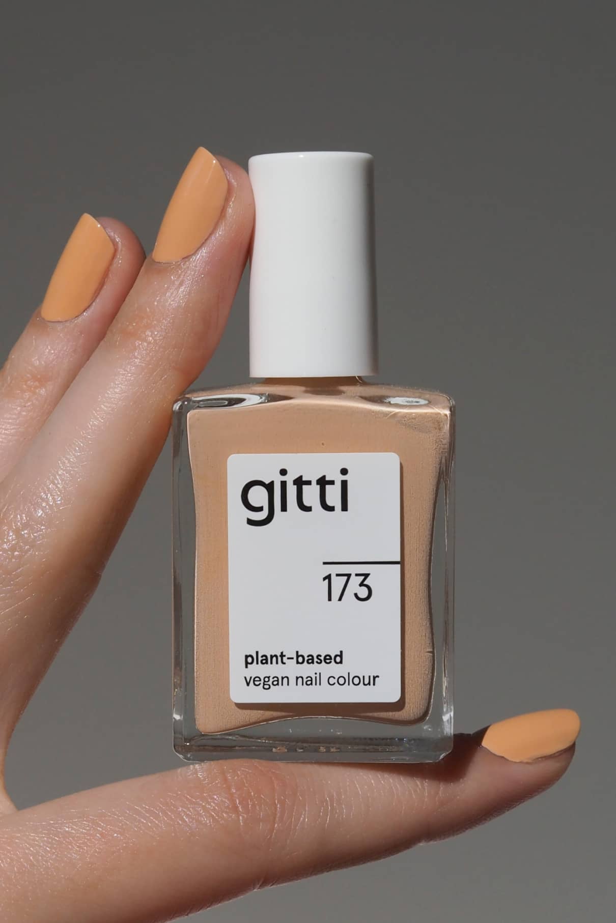 Eine Hand mit pfirsichfarbenen Nägeln hält eine Flasche von gitti no. 173, einer pflanzlichen veganen Nagelfarbe in einem passenden hellen Apricot-Ton mit warmen Untertönen.