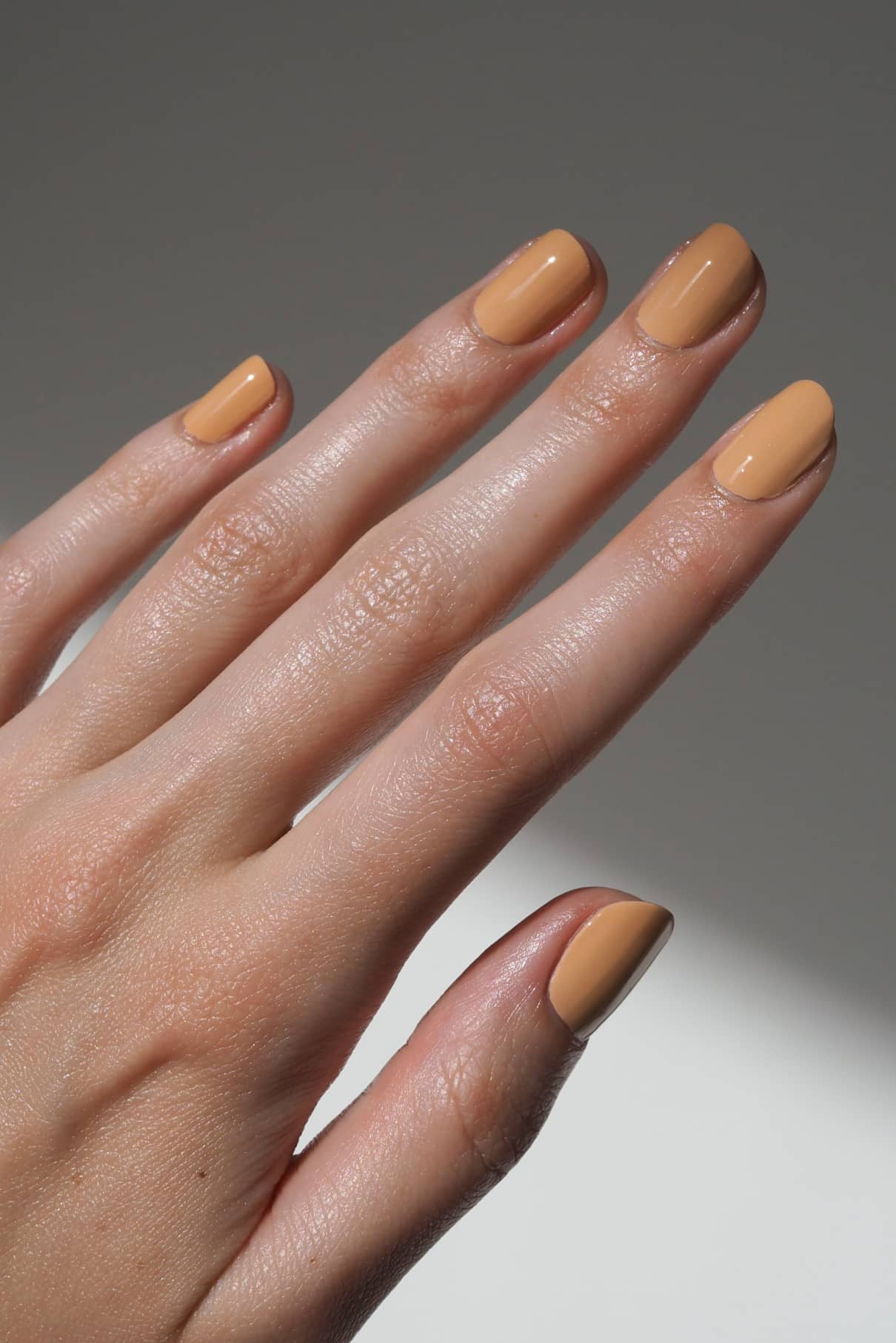 Eine Hand mit sauber manikürten Nägeln, lackiert in gitti no. 173, einem glänzenden, hellen Apricot-Ton mit warmen Untertönen, vor einem neutralen Hintergrund.
