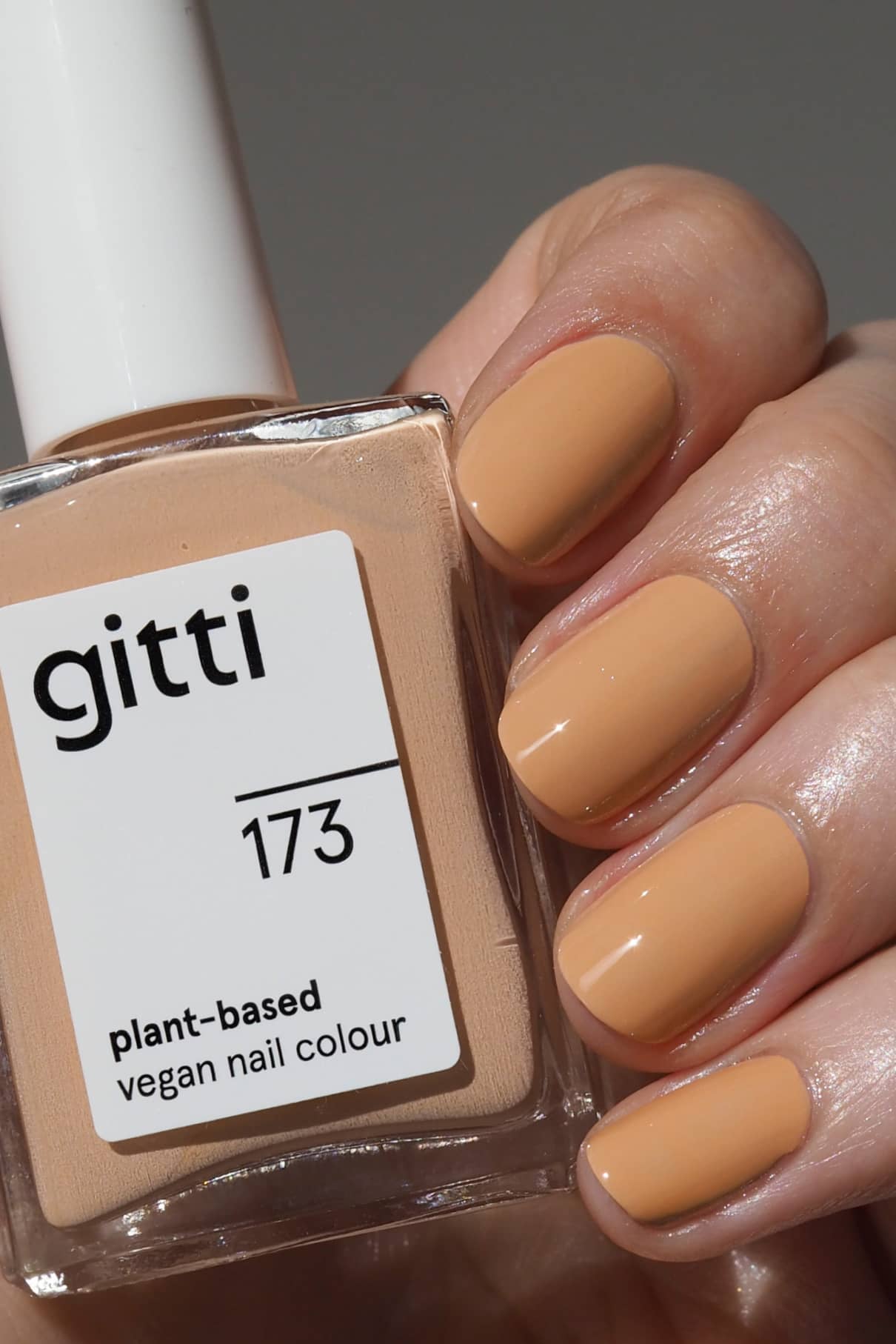 Eine Hand mit sauber manikürten Nägeln in einem hellen Apricot-Ton mit warmen Untertönen hält eine Flasche gitti no. 173, einem veganen Nagellack auf Pflanzenbasis.