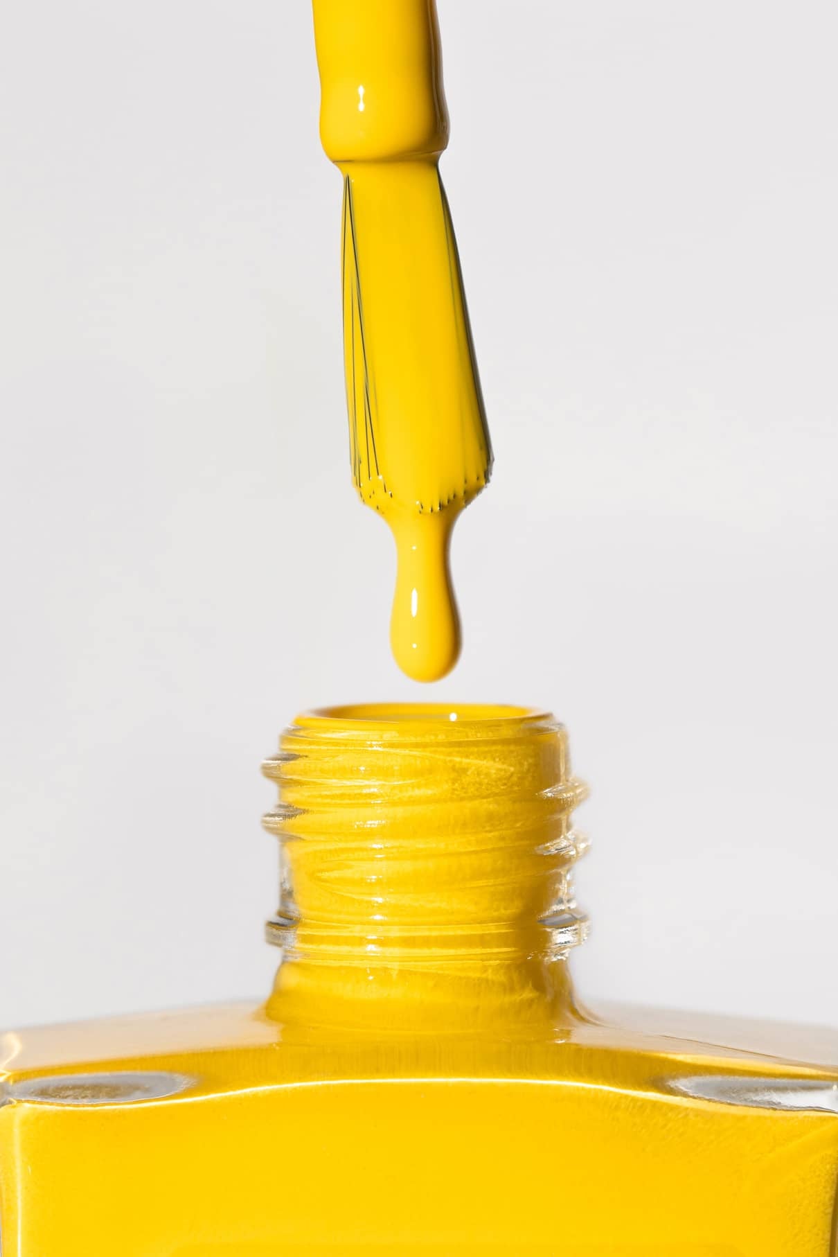 Nahaufnahme eines Pinsels mit gitti no. 175 Nagellack über einer geöffneten gelben Flasche, ein Tropfen bildet sich an der Spitze.