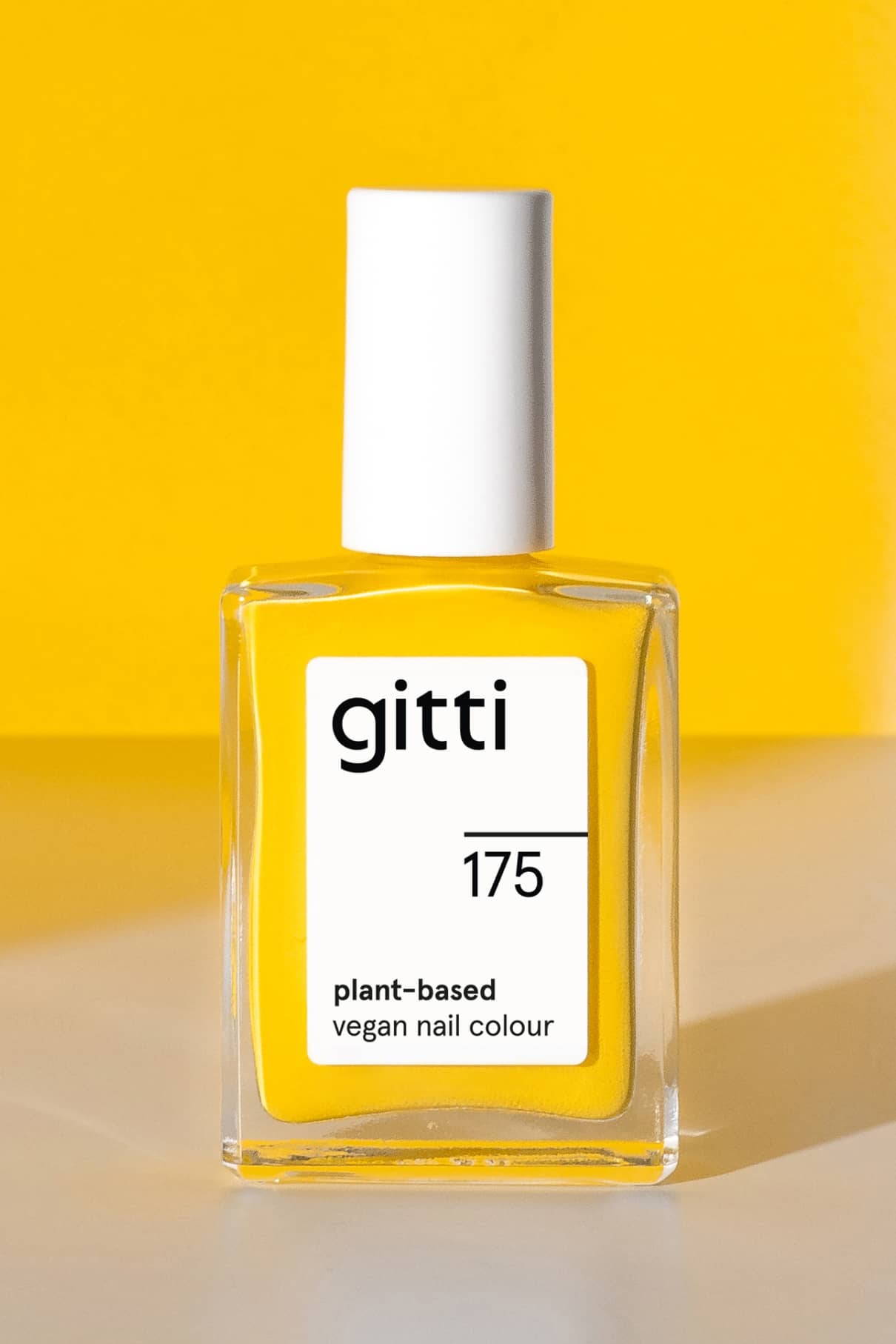 Eine Flasche gitti no. 175 pflanzliche, vegane Nagelfarbe mit weißem Etikett und Kappe auf einem leuchtend gelben Hintergrund.