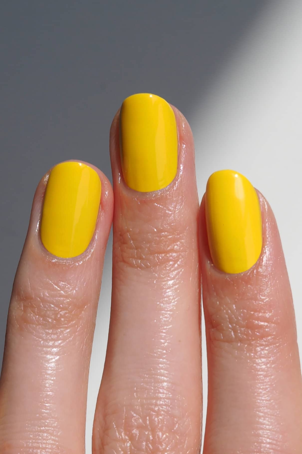 Eine Nahaufnahme von drei Fingern mit kurzen, ovalen Nägeln, die mit gitti no. 175 lackierten Fingernägeln mit glänzendem gelbem Nagellack.