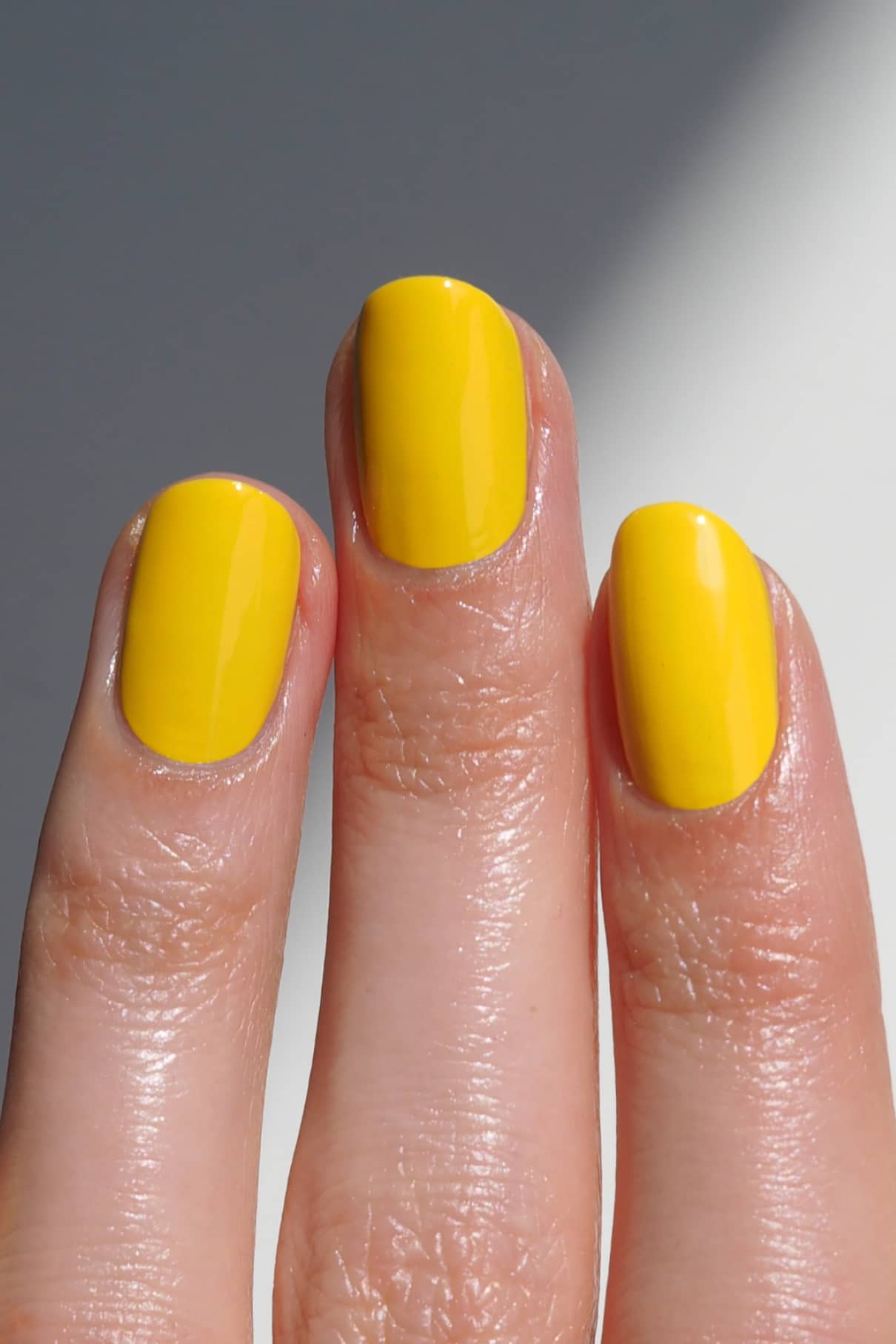Eine Nahaufnahme von drei Fingern mit kurzen, ovalen Nägeln, die mit gitti no. 175 lackierten Fingernägeln mit glänzendem gelbem Nagellack.