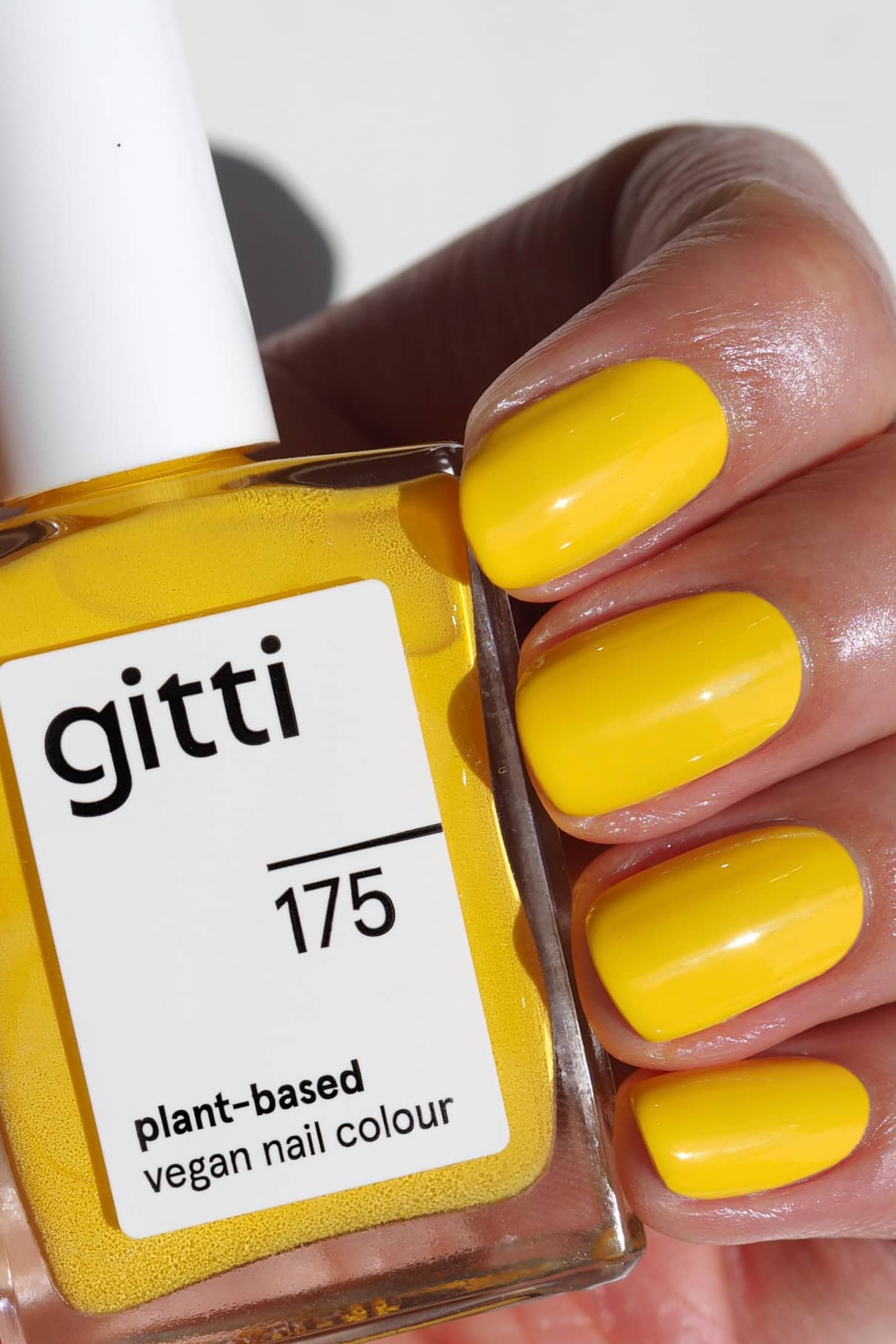 Eine Hand mit sauber manikürten, in leuchtendem Gelb lackierten Nägeln hält eine Flasche gitti no. 175 pflanzlichen veganen Nagellack im passenden Farbton.