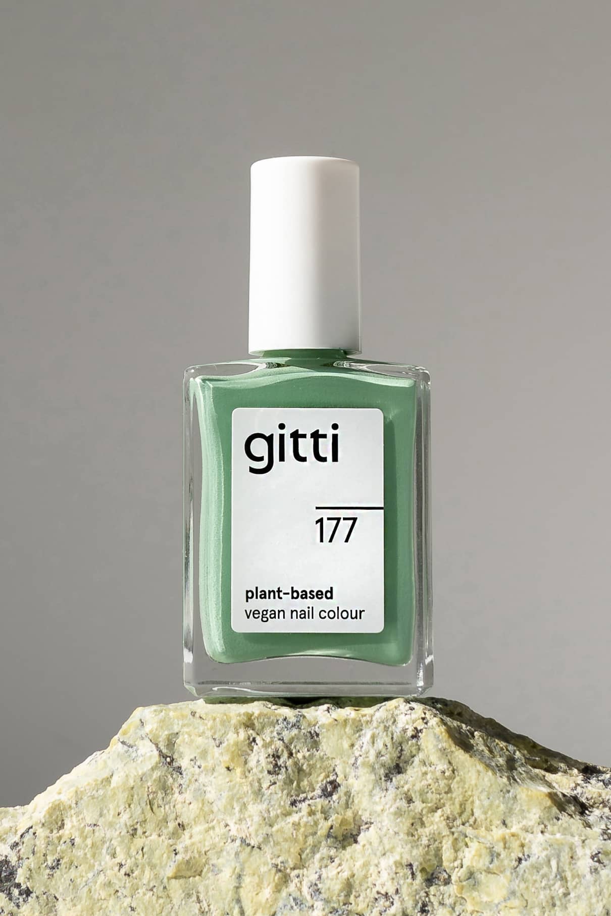 Eine Flasche gitti no. 177 pflanzliche vegane Nagelfarbe in sanfterem Grünton ruht auf strukturiertem Stein vor einem neutralen Hintergrund.