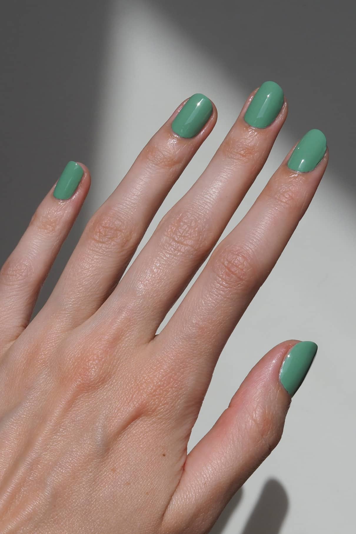 Eine Hand mit sauber manikürten Nägeln, lackiert in gitti no. 177, einem sanften Grünton, vor einem neutralen Hintergrund mit einem leichten Schatten.