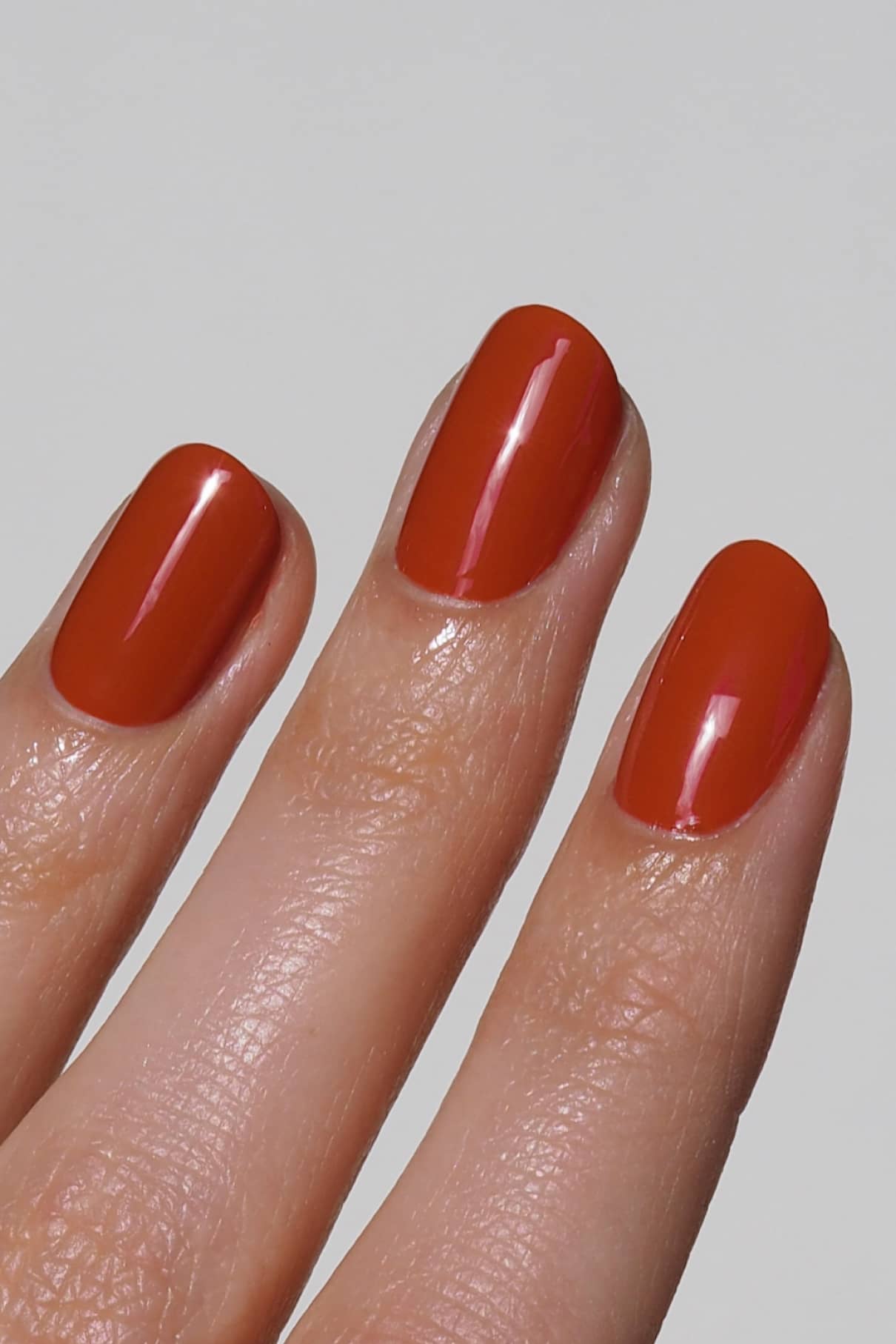 Eine Nahaufnahme von drei Fingern mit kurzen, glänzenden Nägeln, lackiert in gitti no. 178, einem warmen orangeroten Farbton, vor einem schlichten hellen Hintergrund.