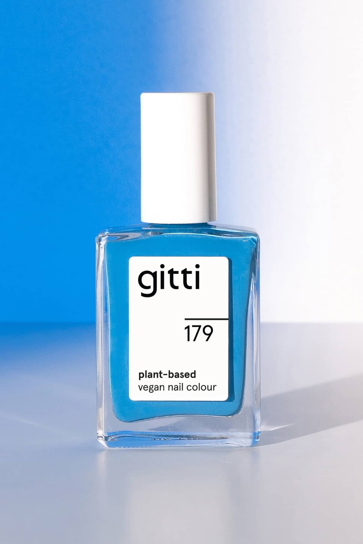 Eine Klarglasflasche mit gitti no. 179 pflanzliche vegane Nagelfarbe in strahlendem Blau mit weißer Kappe, dargestellt auf blauem und weißem Hintergrund.