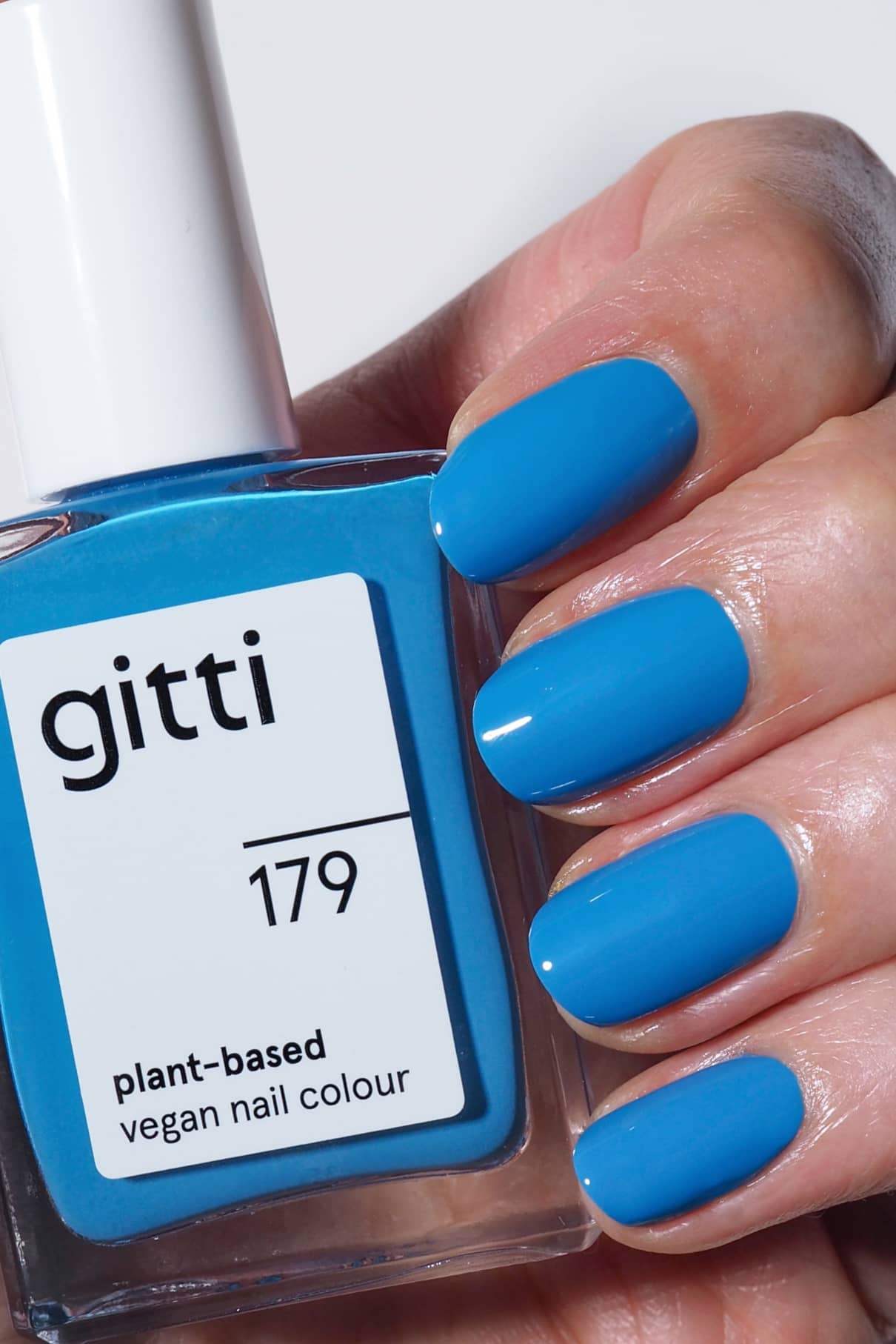 Eine Hand mit blau lackierten Nägeln hält eine Flasche gitti no. 179 pflanzlichen veganen Nagellack, der perfekt zu dem leuchtenden Farbton passt.