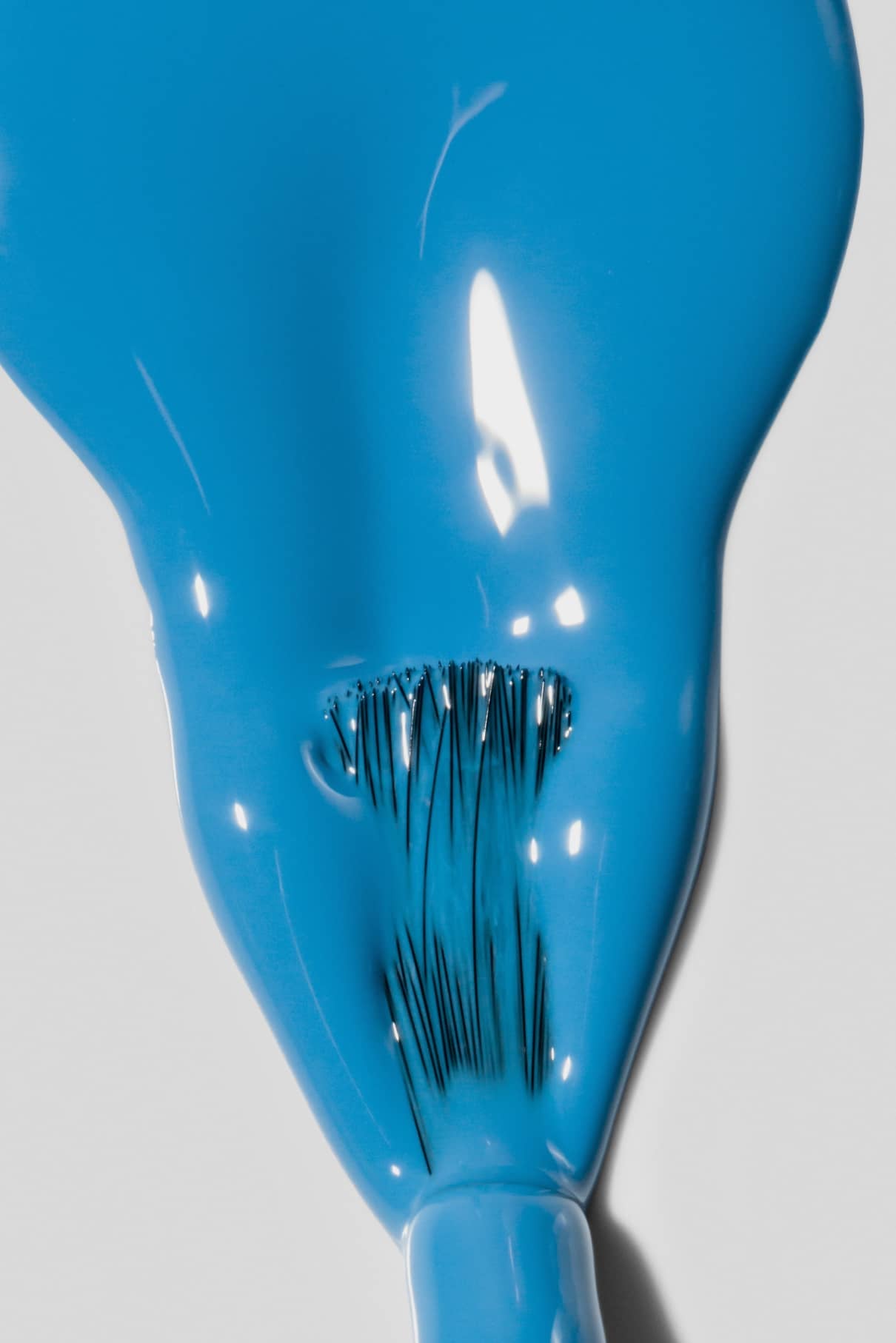 Nahaufnahme eines Pinsels, der mit gitti no. 179, mit sichtbaren Borsten, die den leuchtenden Farbton strahlendes Blau auf einer glatten, hellen Oberfläche verteilen.