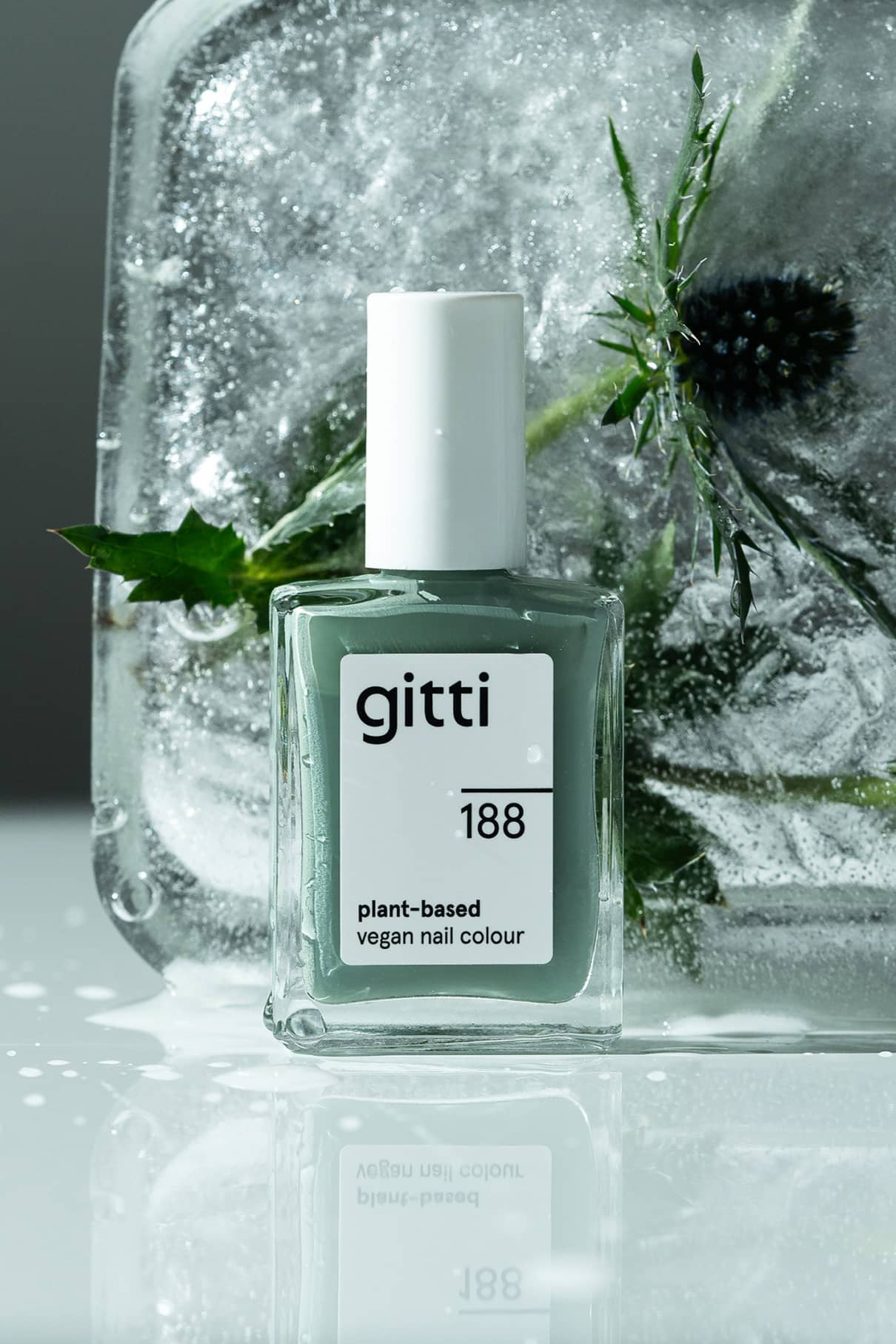 Eine Flasche gitti no. 188 pflanzliche vegane Nagelfarbe steht vor einem Eisblock mit grünen Blättern und einer Distel, daneben Community-Favorit no. 121 Salbeigrün.