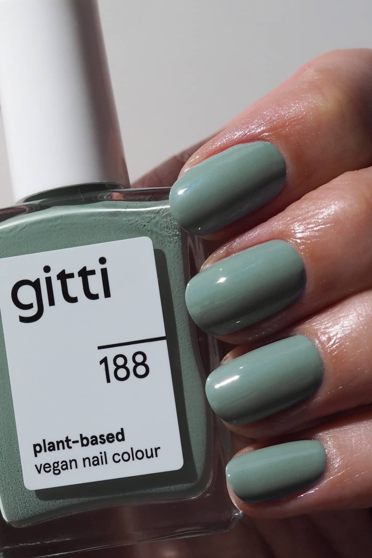 Eine Hand mit kurzen, ovalen, in Salbeigrün lackierten Nägeln hält eine Flasche gitti no. 188 pflanzlicher veganer Nagelfarbe im gleichen Farbton - ein echter Community-Favorit.
