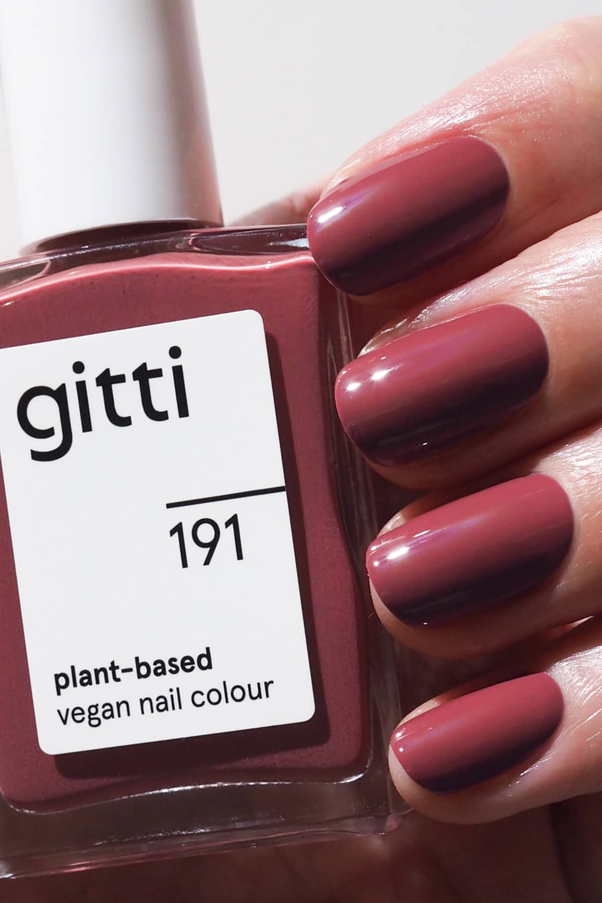 Eine Hand zeigt frisch lackierte Nägel in einem mauvefarbenen Beerenrosa-Ton und hält eine Flasche gitti no. 191 pflanzlicher veganer Nagellack.