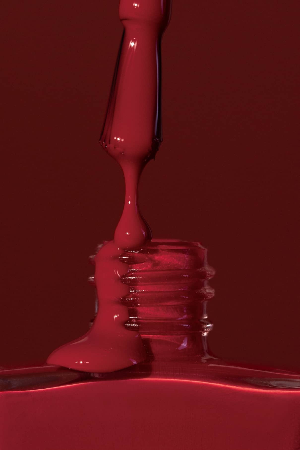 Nahaufnahme eines Nagellackpinsels, der Gitti Nr. 192 in eine offene Glasflasche vor einem passenden roten Hintergrund.
