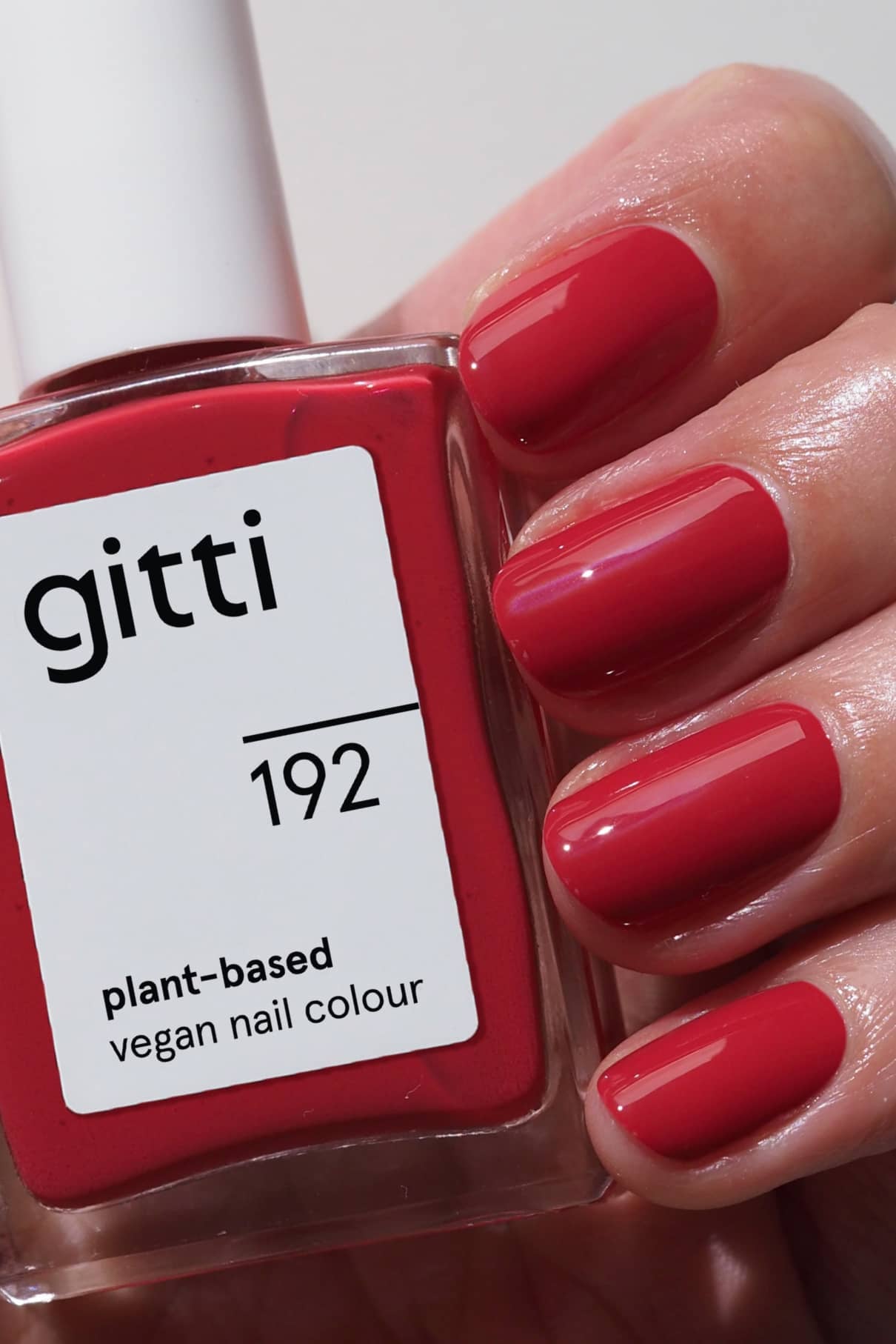 Eine Hand mit sauber manikürten, in einem leuchtendes Rot lackierten Nägeln hält eine Flasche gitti no. 192 vegane Nagelfarbe auf Pflanzenbasis.