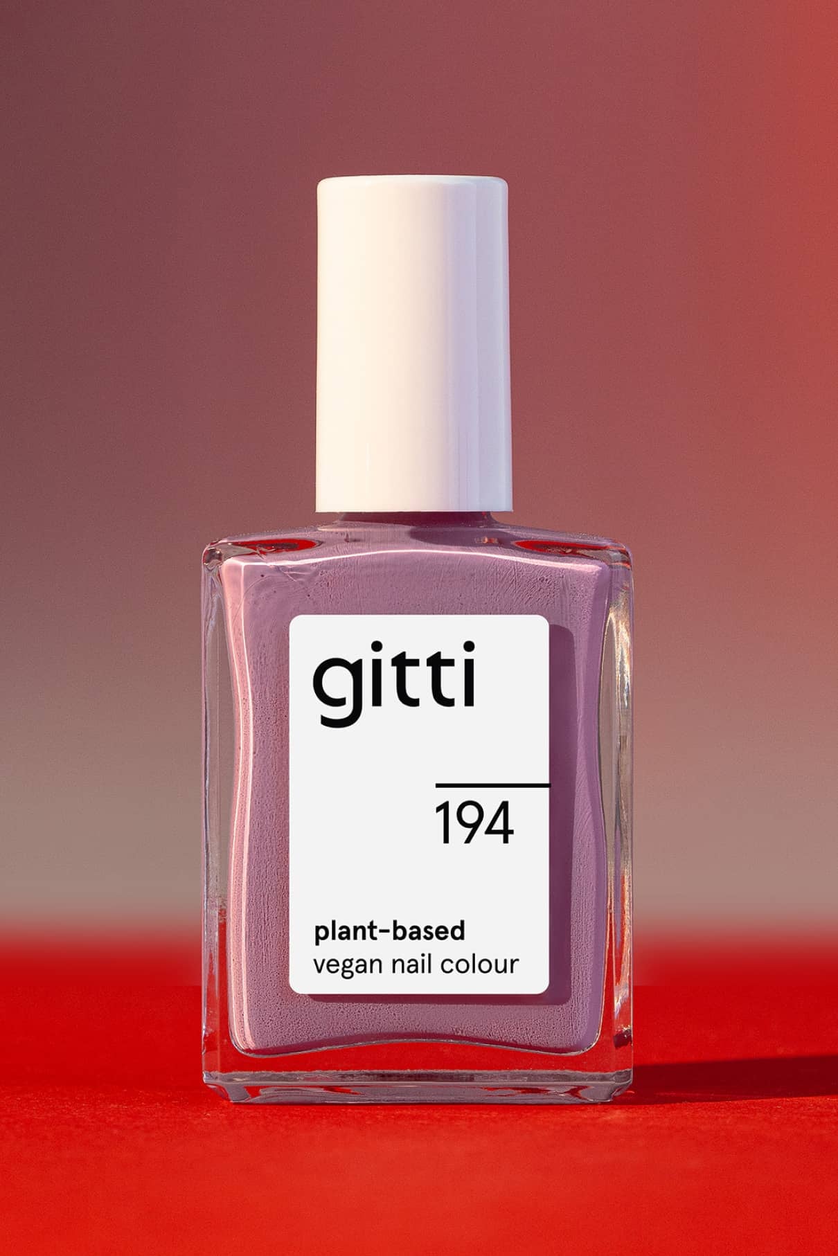 Eine Flasche gitti no. 194 pflanzlicher veganer Nagellack in zartem Mauve mit einem Hauch von Blau, weiße Kappe, auf rotem und rosa Hintergrund.