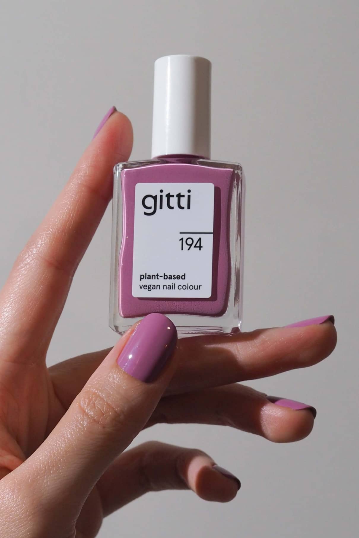 Eine Hand hält eine Flasche mit gitti no. 194 pflanzlicher veganer Nagellack in zartem Mauve mit blauen Untertönen, mit perfekt passendem Lack auf den Nägeln.