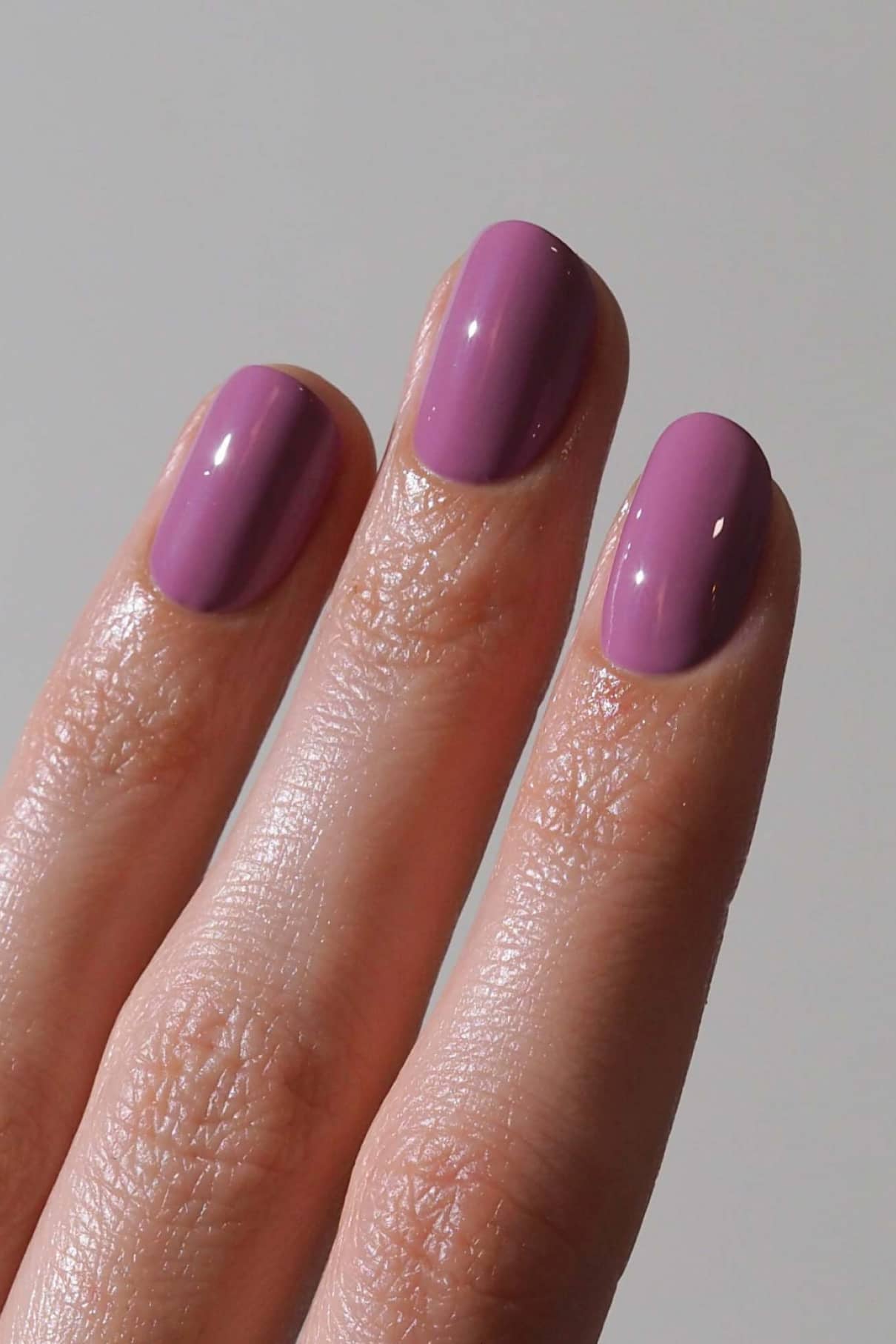 Eine Nahaufnahme von drei Fingern mit sauber manikürten Nägeln, die mit gitti no. 194 lackierten Fingernägeln, die eine glänzende mauve Farbe mit einem subtilen blauen Unterton aufweisen.