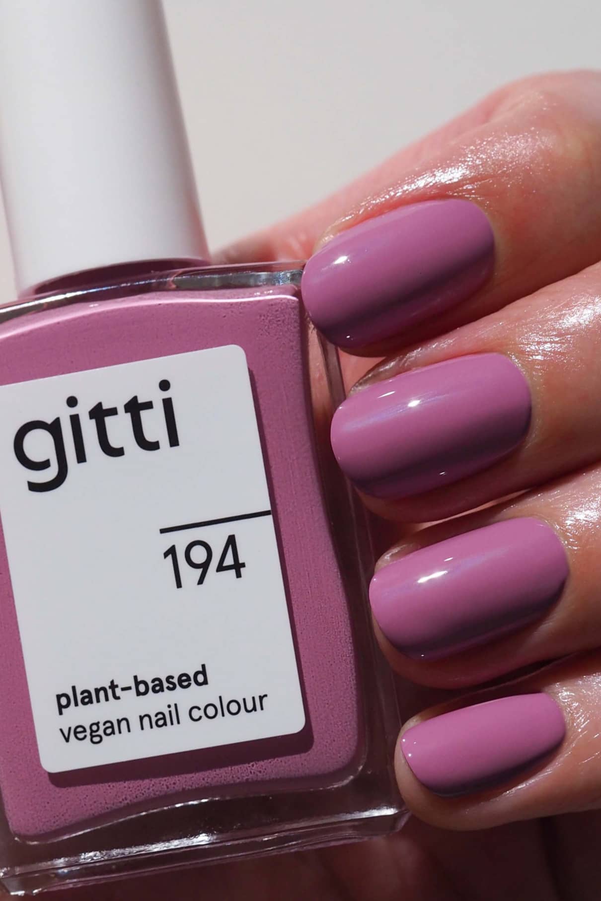 Eine Hand mit kurzen, sauber manikürten Nägeln, die in zartem Mauve mit blauem Unterton lackiert sind, hält eine Flasche gitti no. 194 pflanzlicher veganer Nagellack im passenden Farbton.