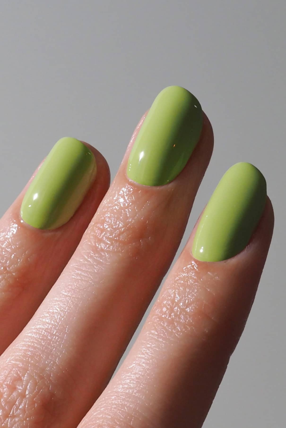 Nahaufnahme von drei Fingern mit glattem, glänzendem gitti no. 196 Nagellack in harmonischem Grün vor einem schlichten, neutralen Hintergrund.