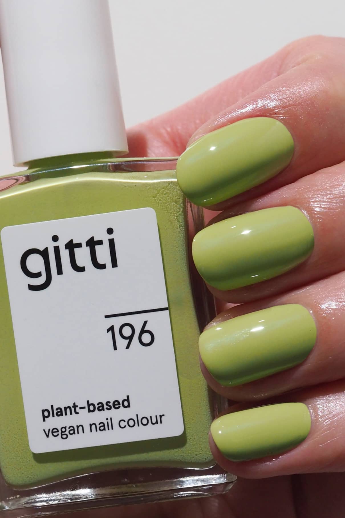 Eine Hand mit mittellang lackierten Nägeln in frischem Grün hält eine Flasche gitti no. 196, einer veganen Nagelfarbe auf Pflanzenbasis.