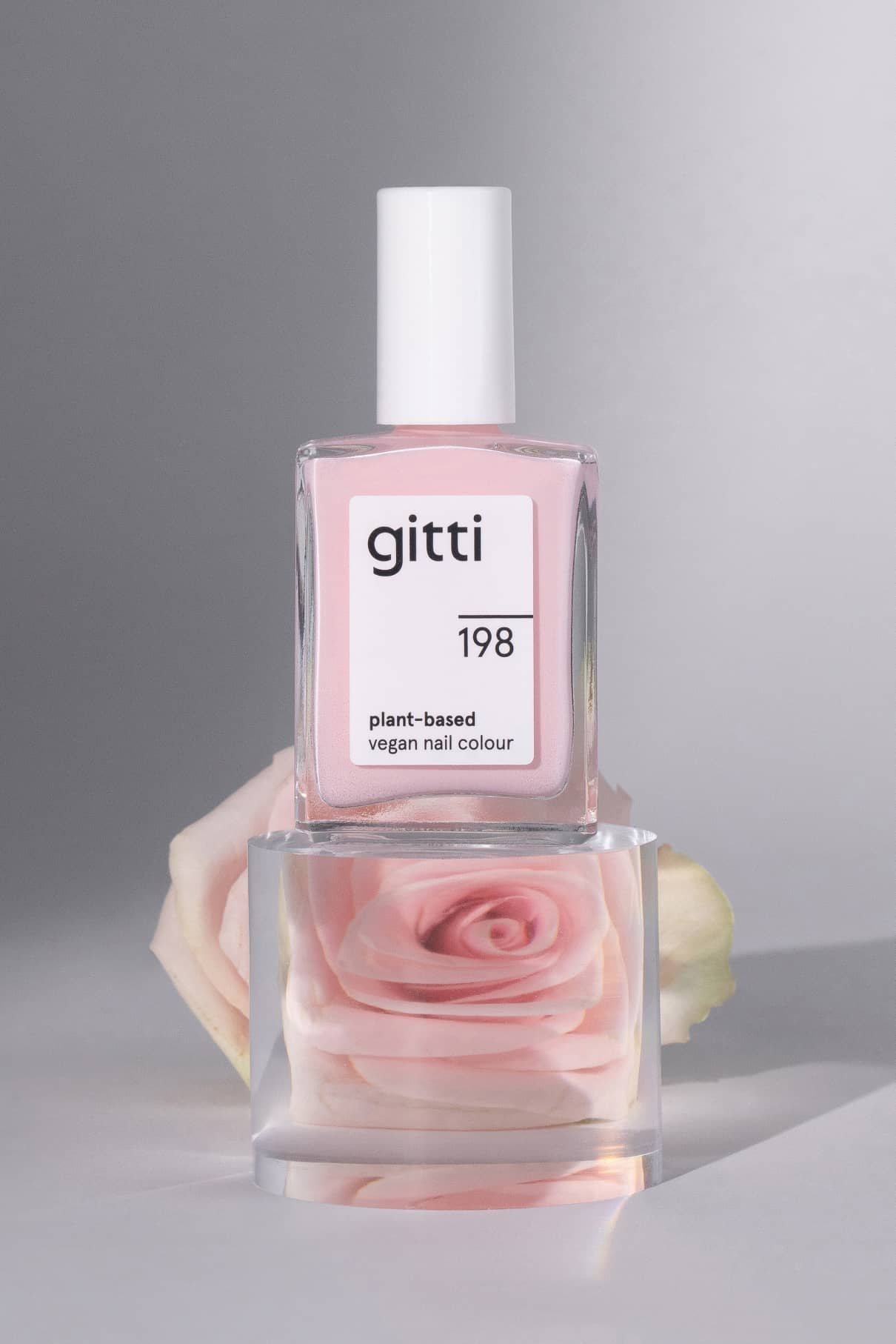 Eine Flasche von gitti no. 198, eine vegane Nagelfarbe auf pflanzlicher Basis in kühlem Pink, ist auf einem durchsichtigen Block mit einer hellrosa Rose im Inneren ausgestellt.
