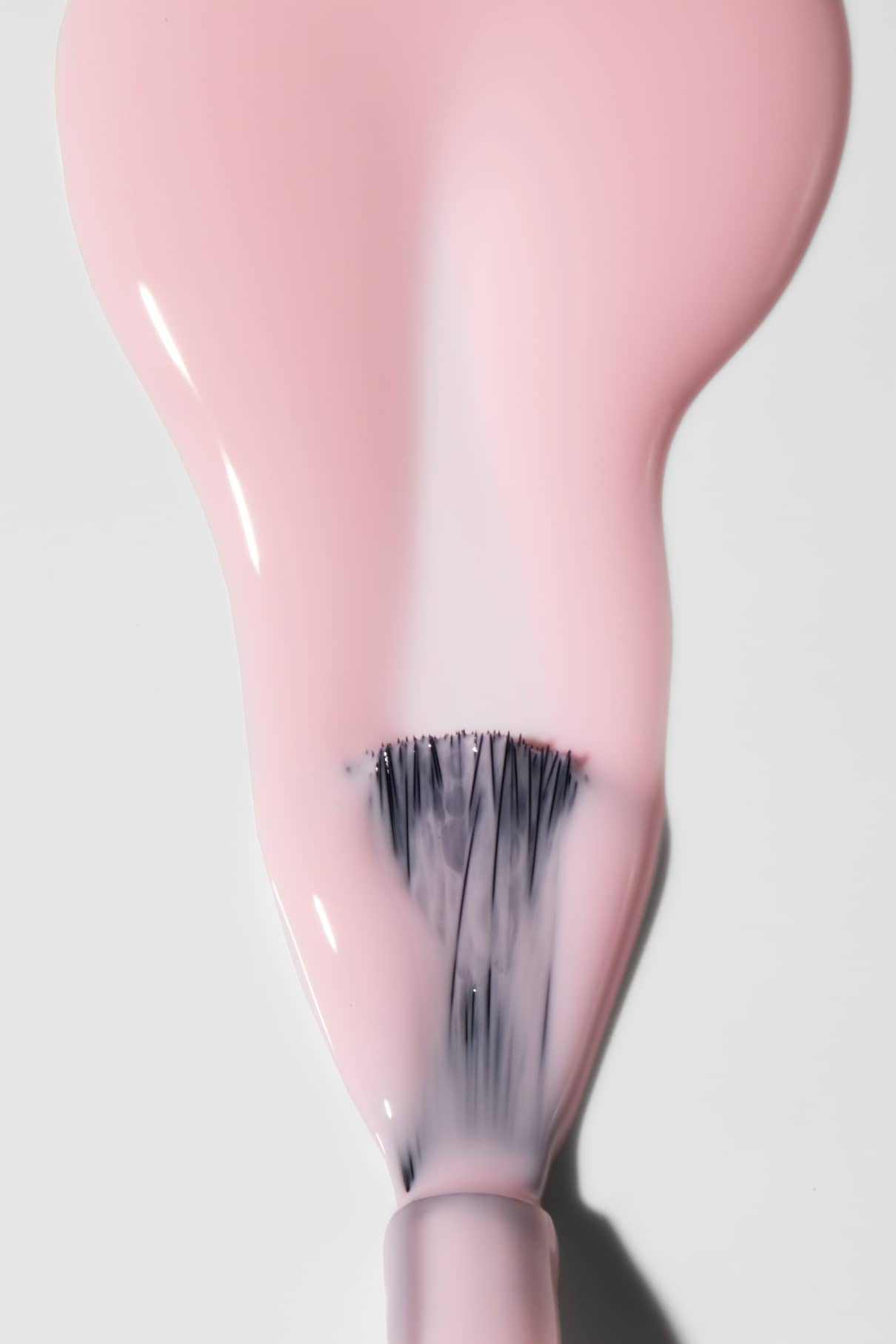 Eine Nahaufnahme eines Pinsels, mit dem gitti no. 198 Nagellack auf. Der hellrosa Farbton verteilt sich gleichmäßig auf einer weißen Fläche.