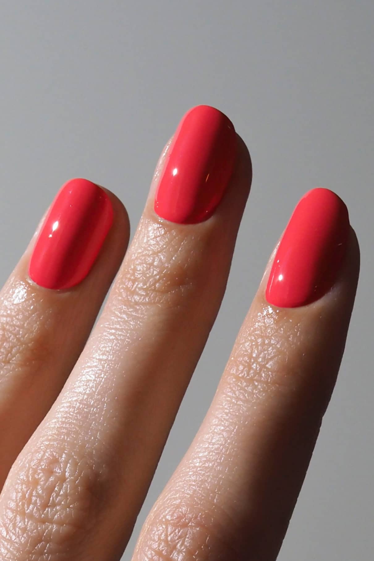 Nahaufnahme von drei Fingern mit glänzendem, hellrosa Nagellack - Gitti Nr. 199, eine leuchtende Mischung aus Rosa und Rot, vor einem schlichten grauen Hintergrund.