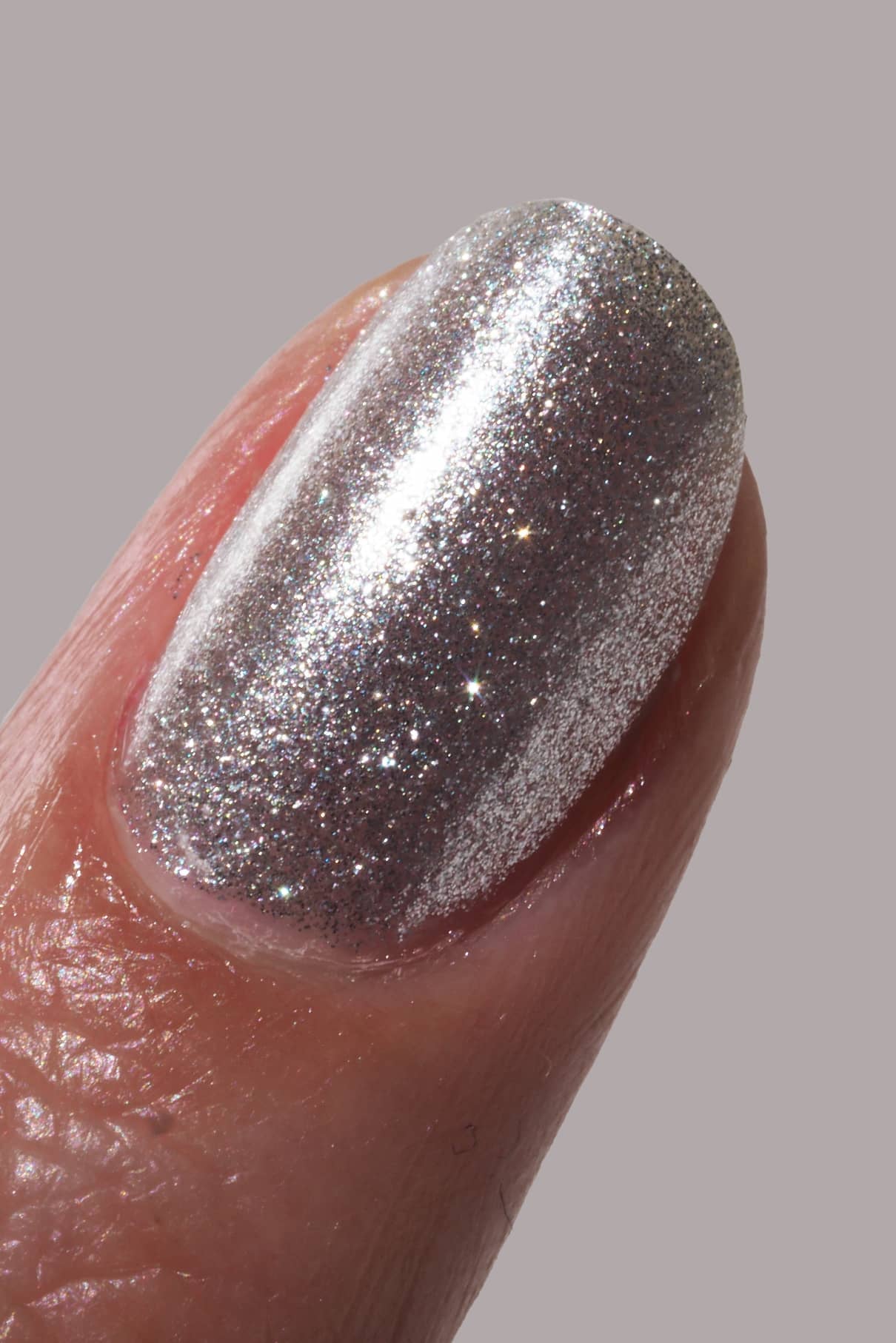 Eine Nahaufnahme eines Fingernagels, der mit glänzendem gitti no. 201 Glitzernagellack lackierten Fingernagels vor einem schlichten Hintergrund.