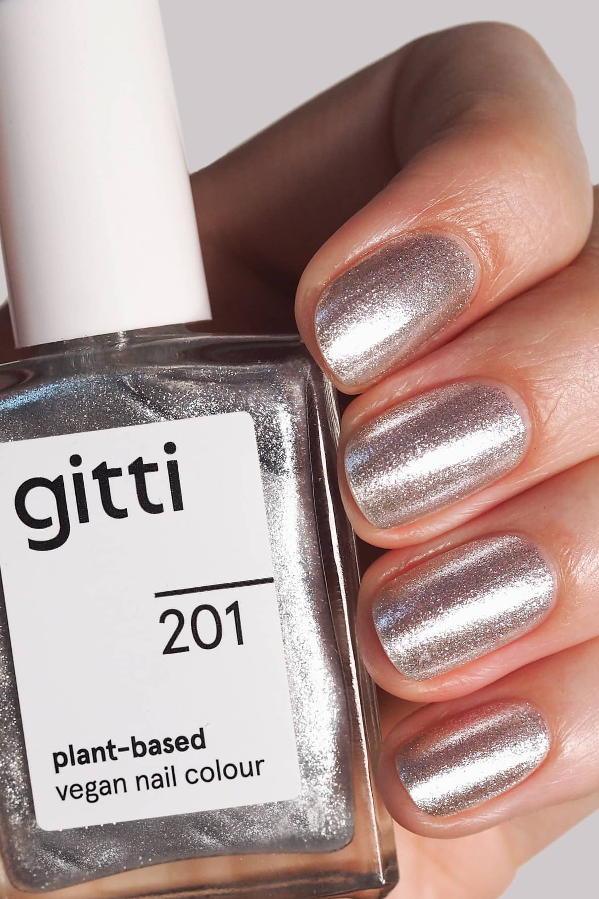 Eine Hand mit kühler Silberton Metallic-Nagellack hält eine Flasche mit der Aufschrift gitti no. 201 vegane Nagelfarbe auf Pflanzenbasis.
