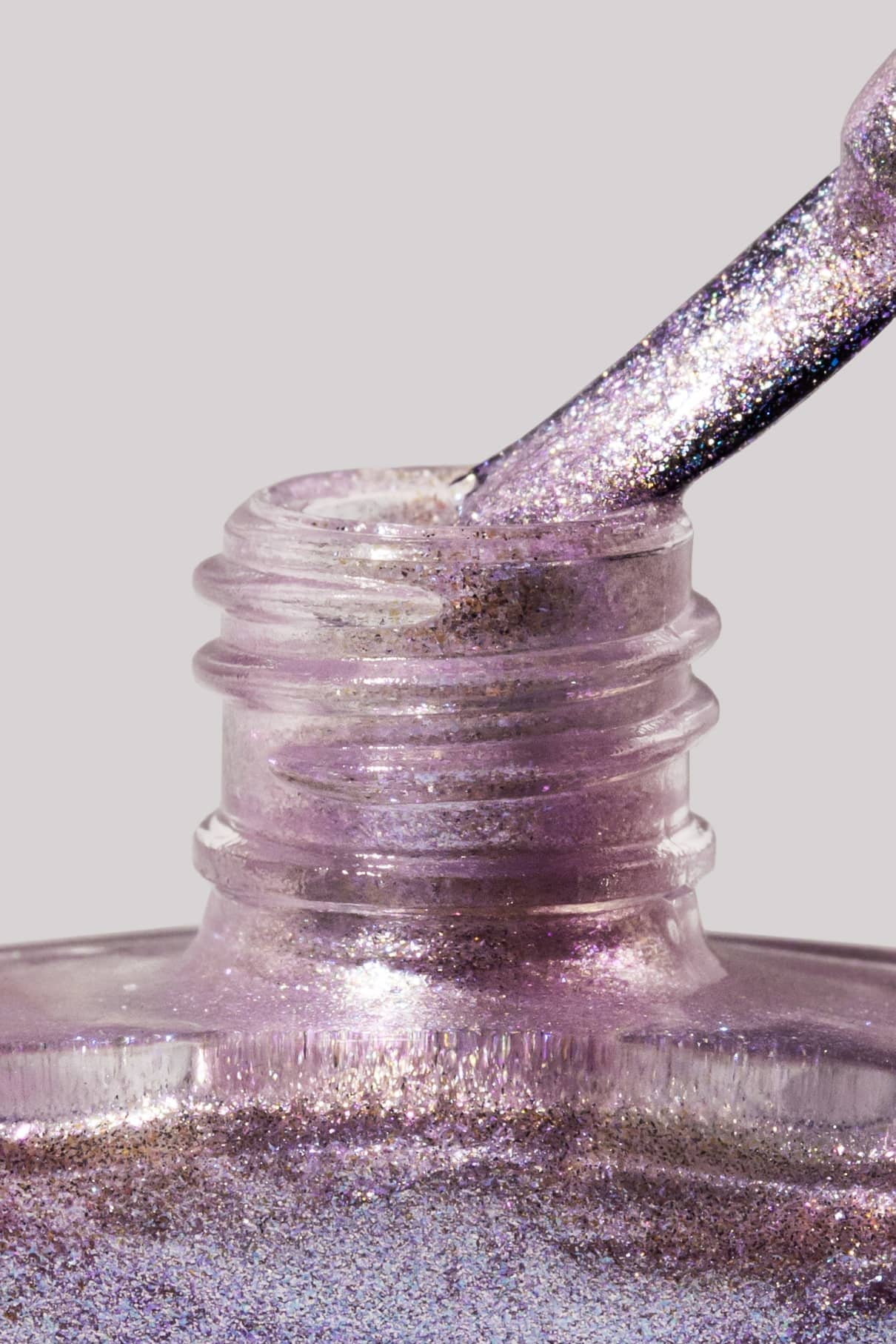 Nahaufnahme von gitti no. 202 Nagellackflasche mit Pinsel, getaucht in schimmerndes, mehrfarbiges Lavendel-Metallic-Lila vor neutralem Hintergrund.