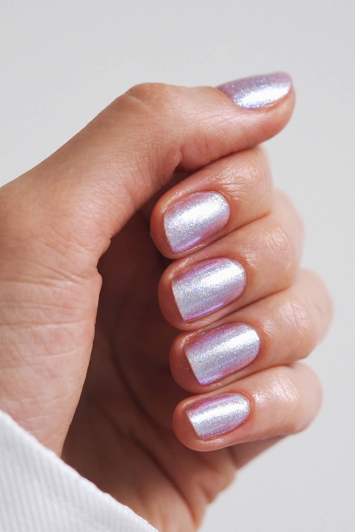 Eine Hand mit kurzen, sauber manikürten Nägeln, lackiert mit gitti no. 202, einem schimmernden, mehrfarbigen lavendelfarbenen Nagellack.
