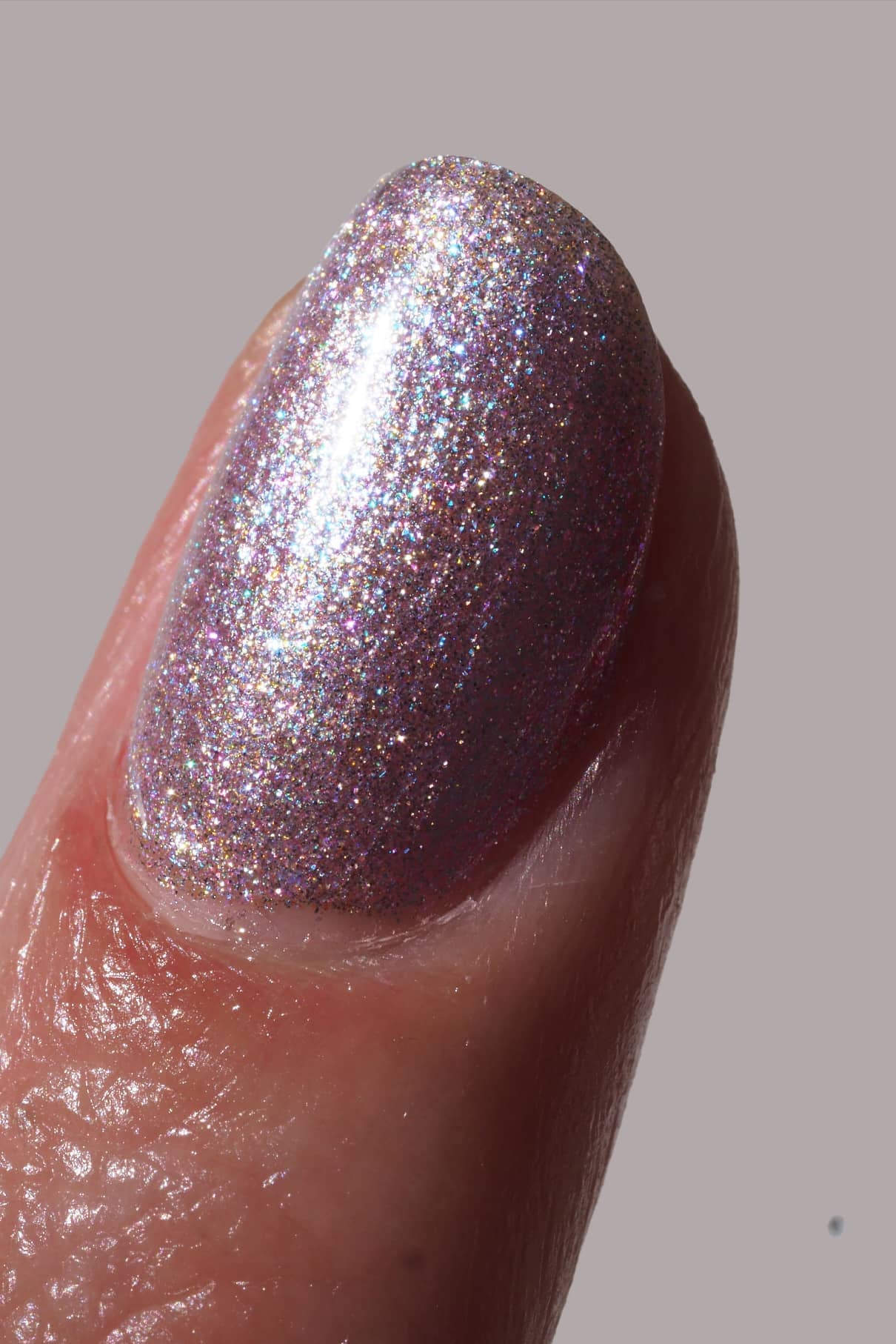 Nahaufnahme eines Fingernagels, der mit gitti no. 202, einem schimmernden, mehrfarbigen lavendelfarbenen Nagellack, vor einem einfarbigen Hintergrund.
