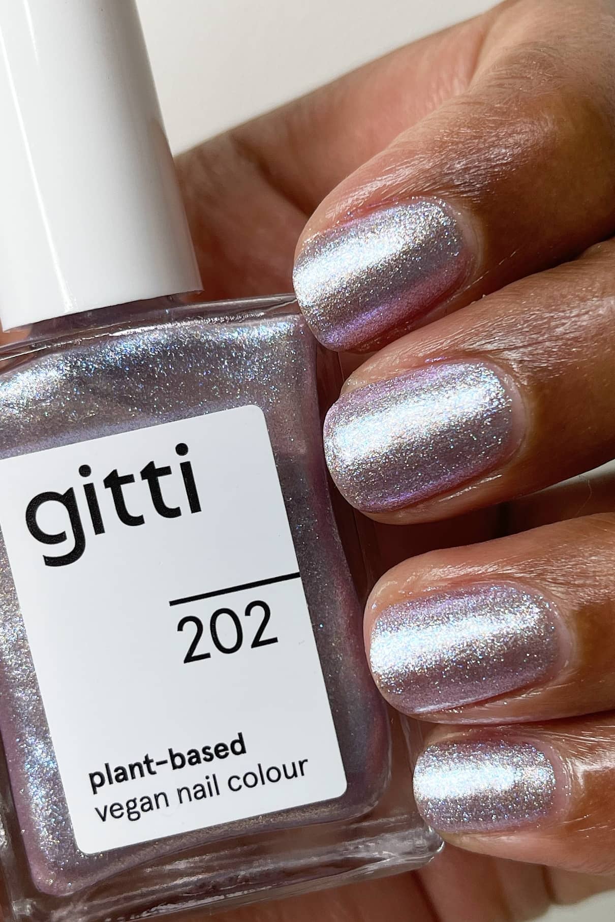 Eine Hand mit silbern schimmernden, irisierenden Nägeln hält ein Fläschchen mit gitti no. 202 pflanzlicher veganer Nagellack im passenden Farbton.