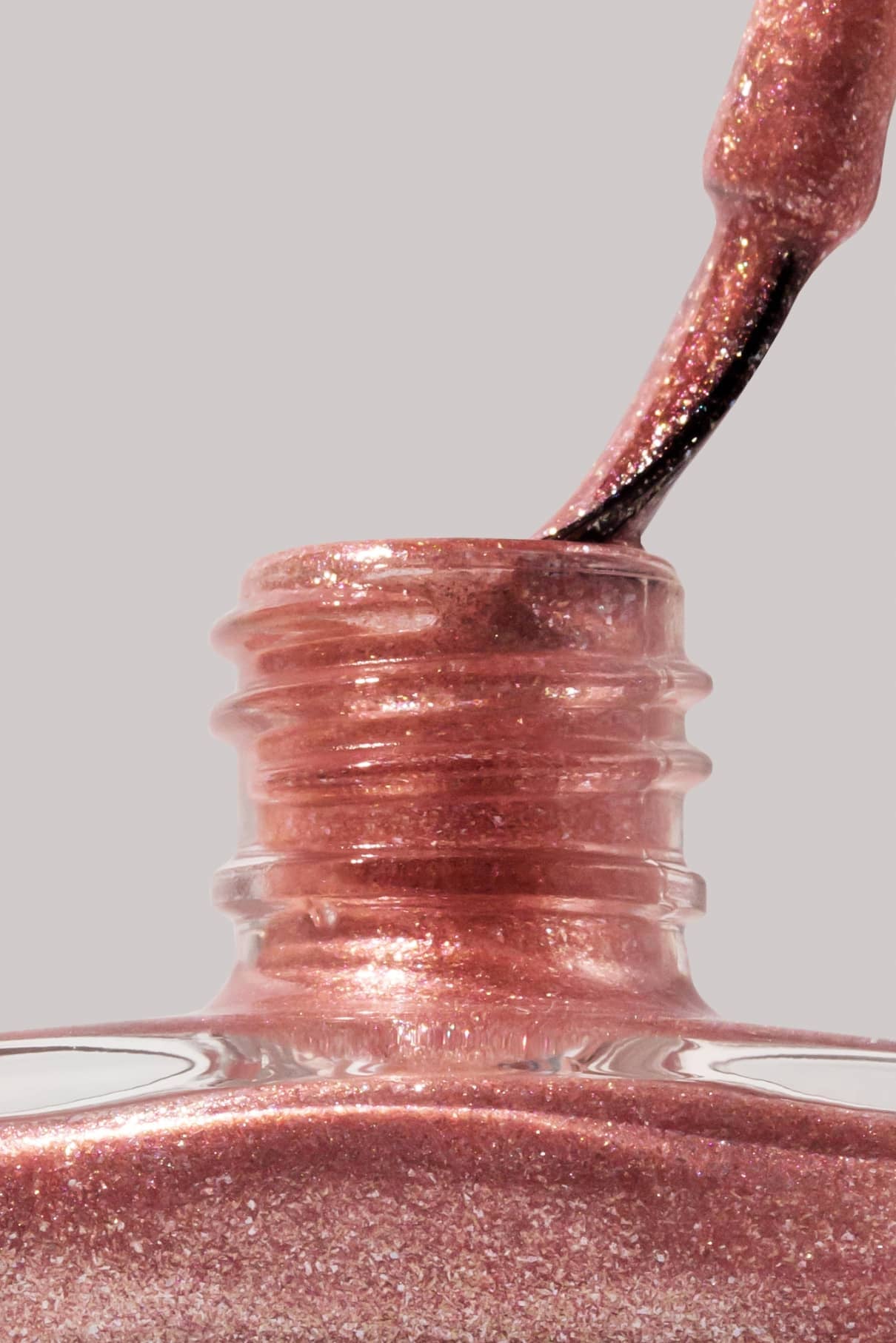 Nahaufnahme eines Pinsels, der in eine offene Flasche mit gitti no. 203, einem schimmernden, kupferfarbenen Nagellack, vor einem neutralen Hintergrund.